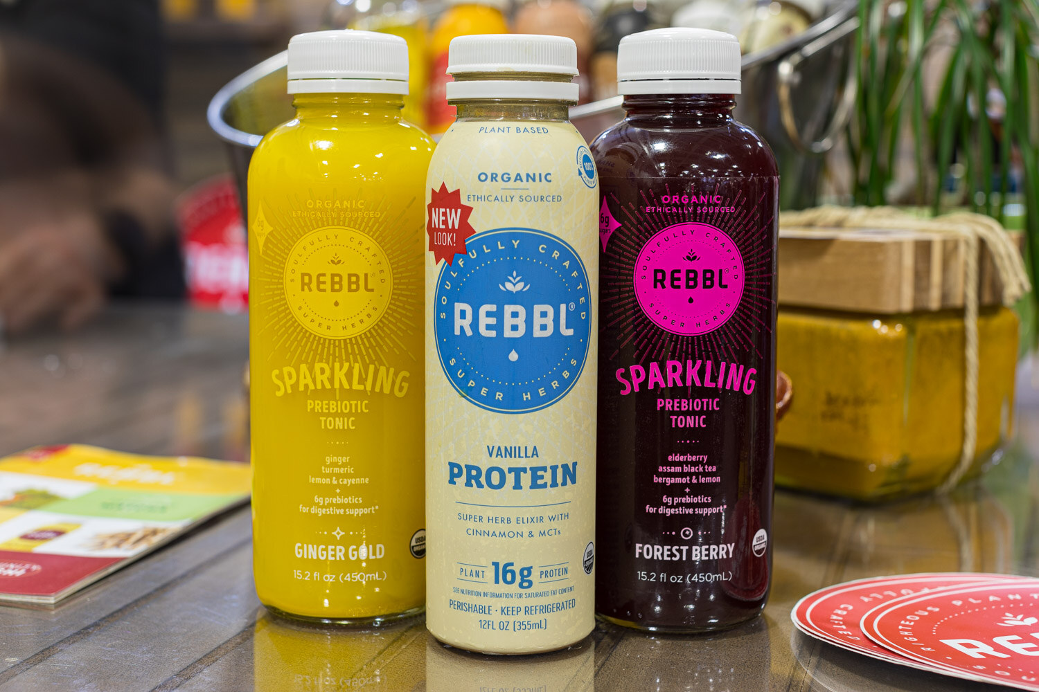 Three REBBL bottles in ginger gold, vanilla protein and forest berry