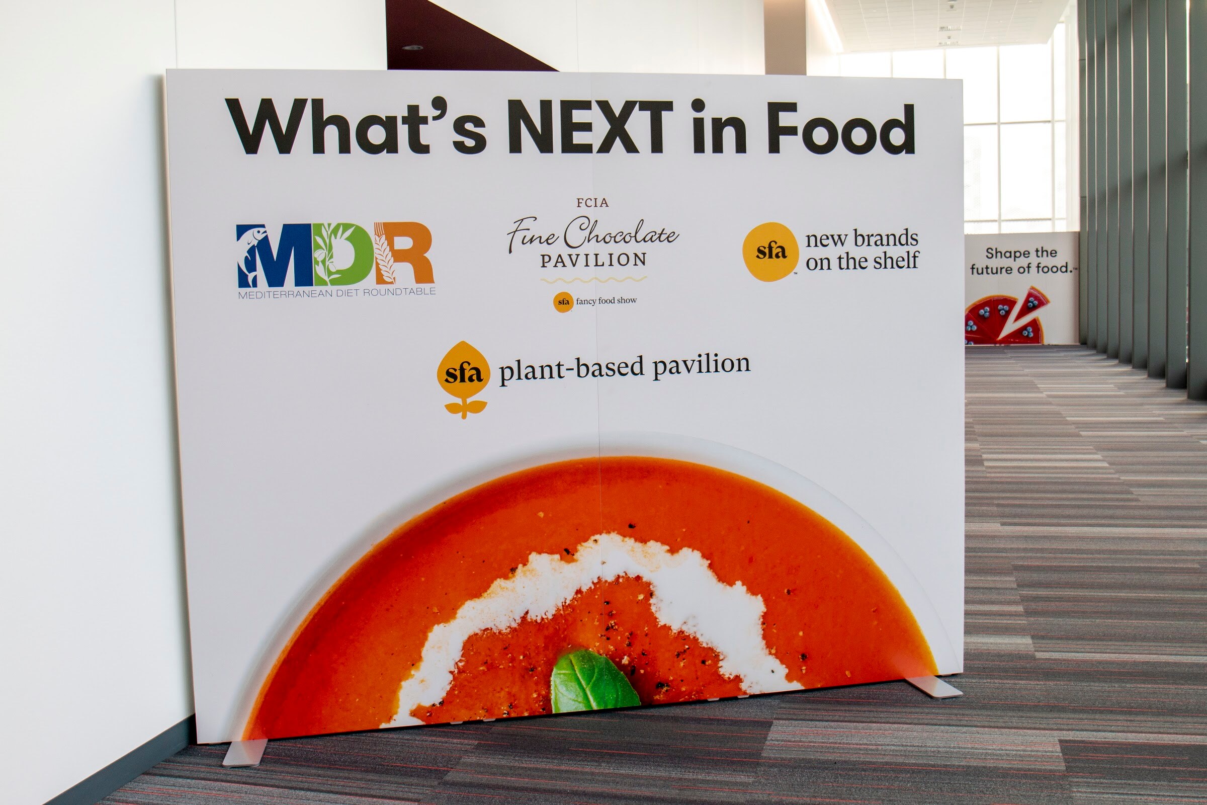 A white sign reading What's NEXT in Food with pavilion logos and an illustration of a bowl of soup