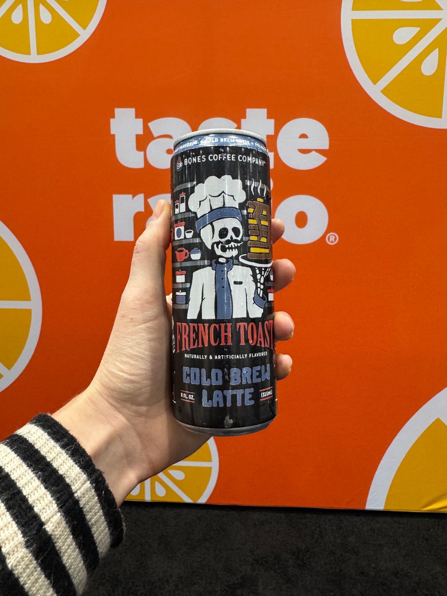 Hand holds a can of Bones Coffee Company French Toast Cold Brew Latte in front of the orange Taste Radio backdrop.