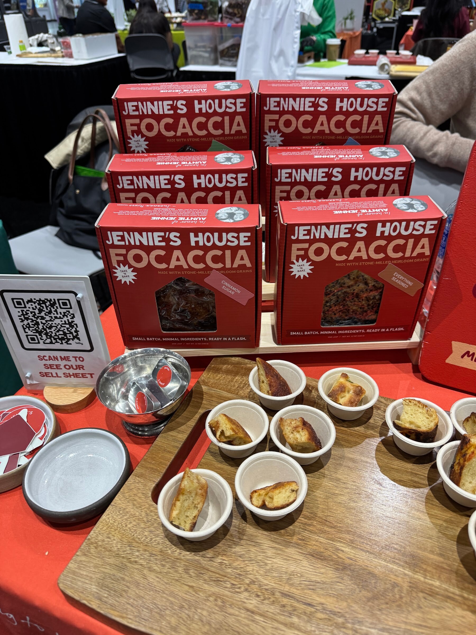 Stacked red boxes of Jennie’s House Focaccia beside a wooden board of focaccia samples.