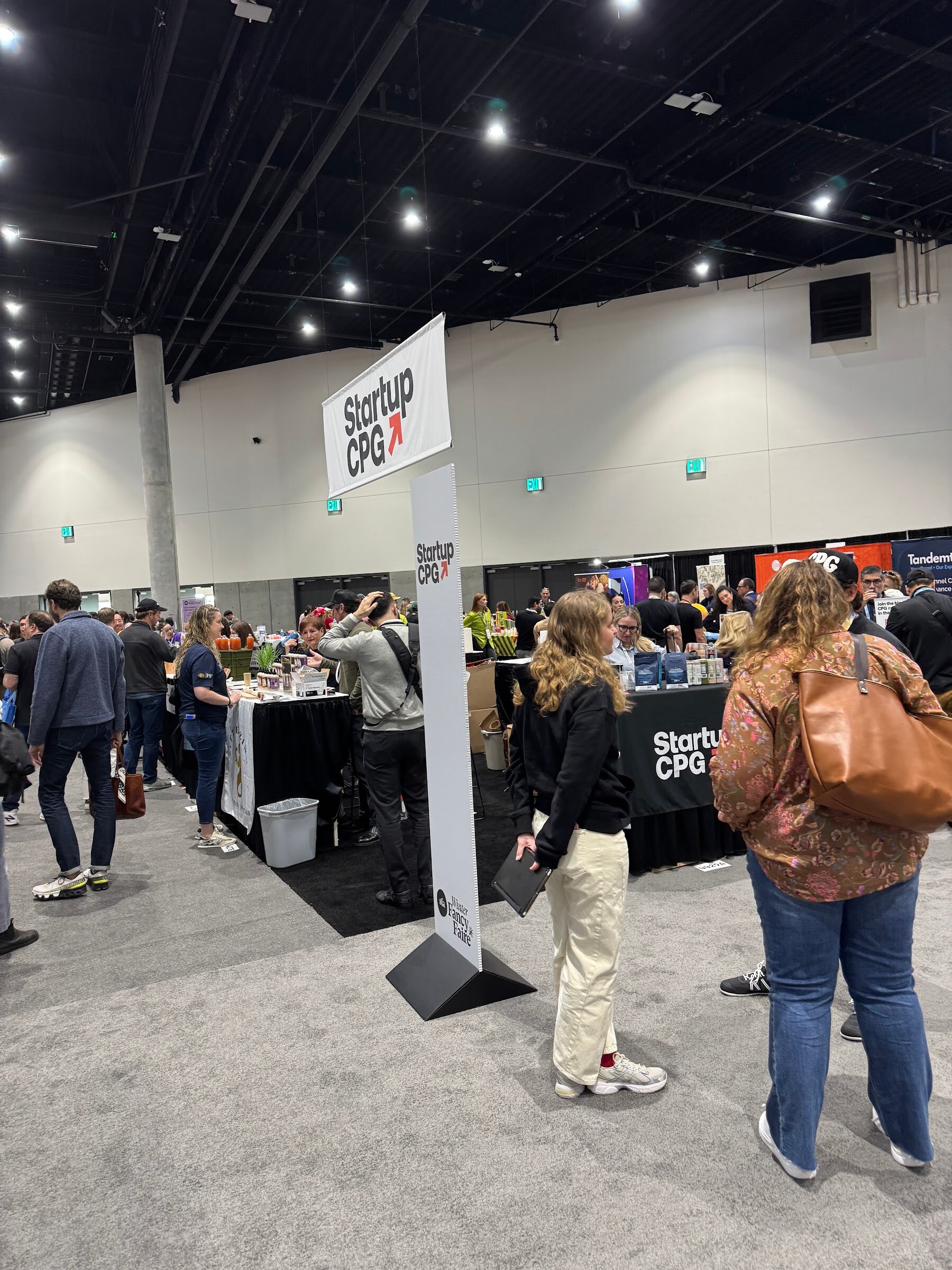 Attendees walk past a Startup CPG sign into an aisle of small brand booths.