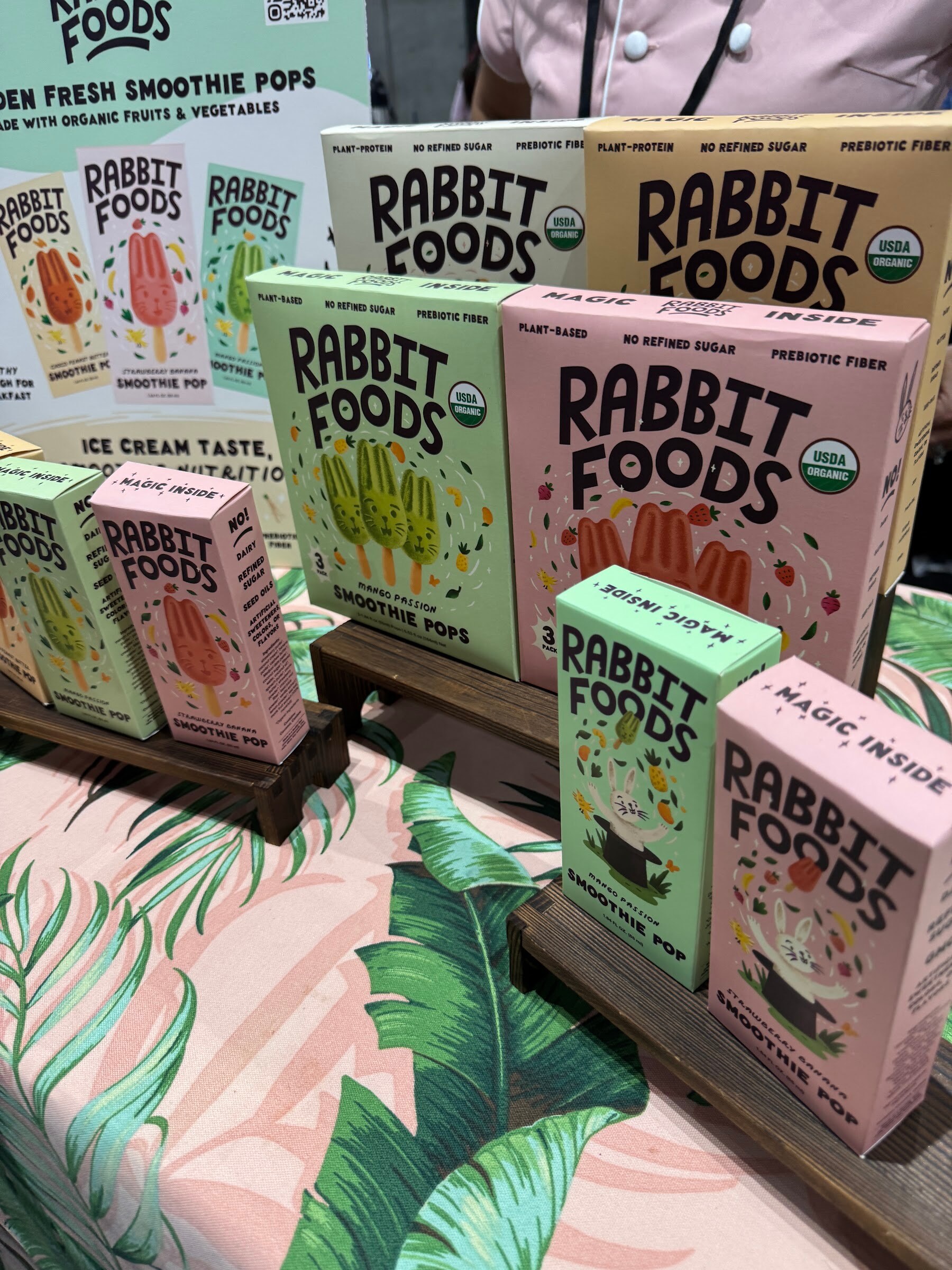 Colorful boxes of Rabbit Foods smoothie pops stacked on a tropical leaf tablecloth.