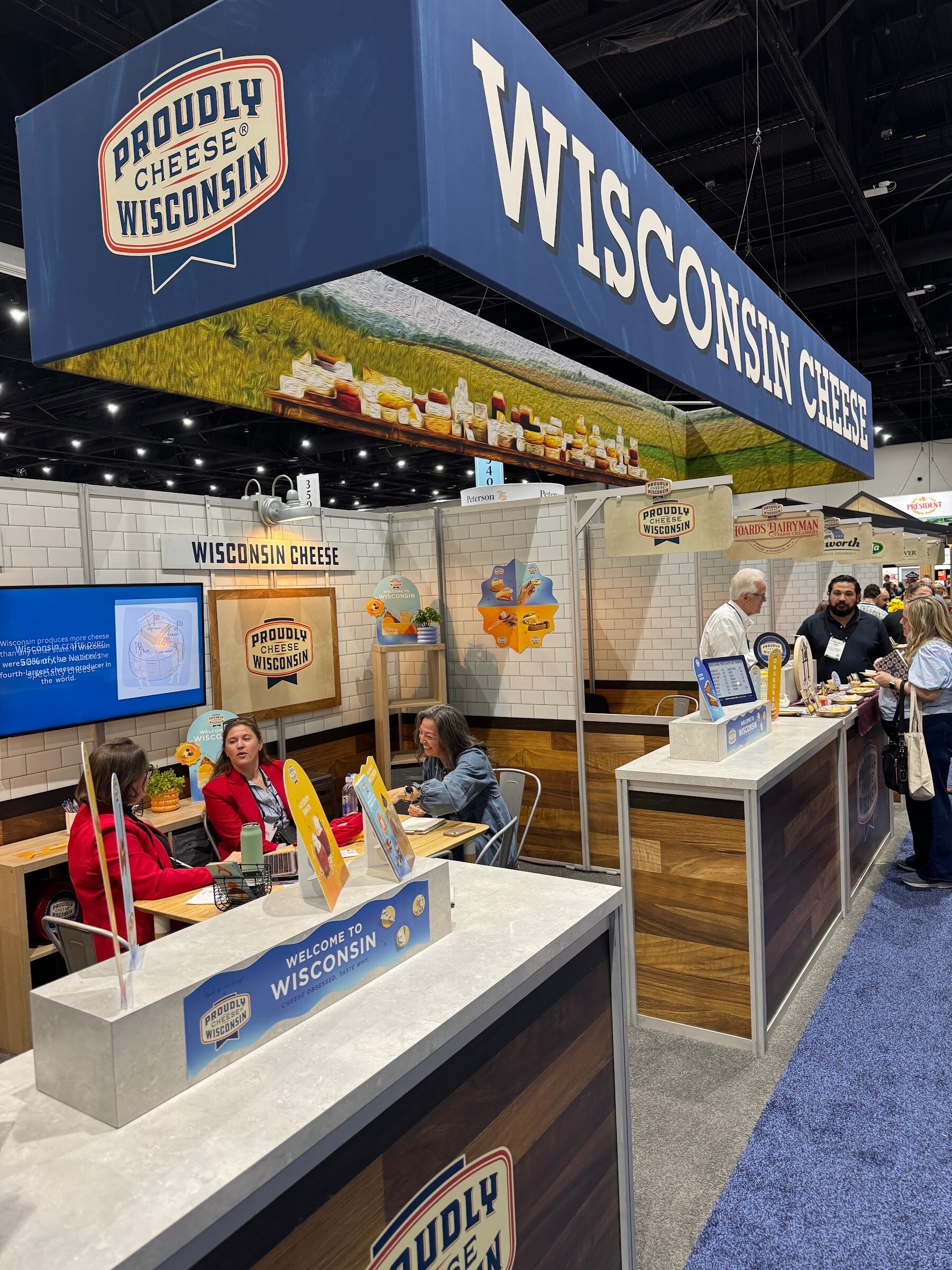 Wisconsin Cheese pavilion with a large blue overhead sign and attendees at counters.