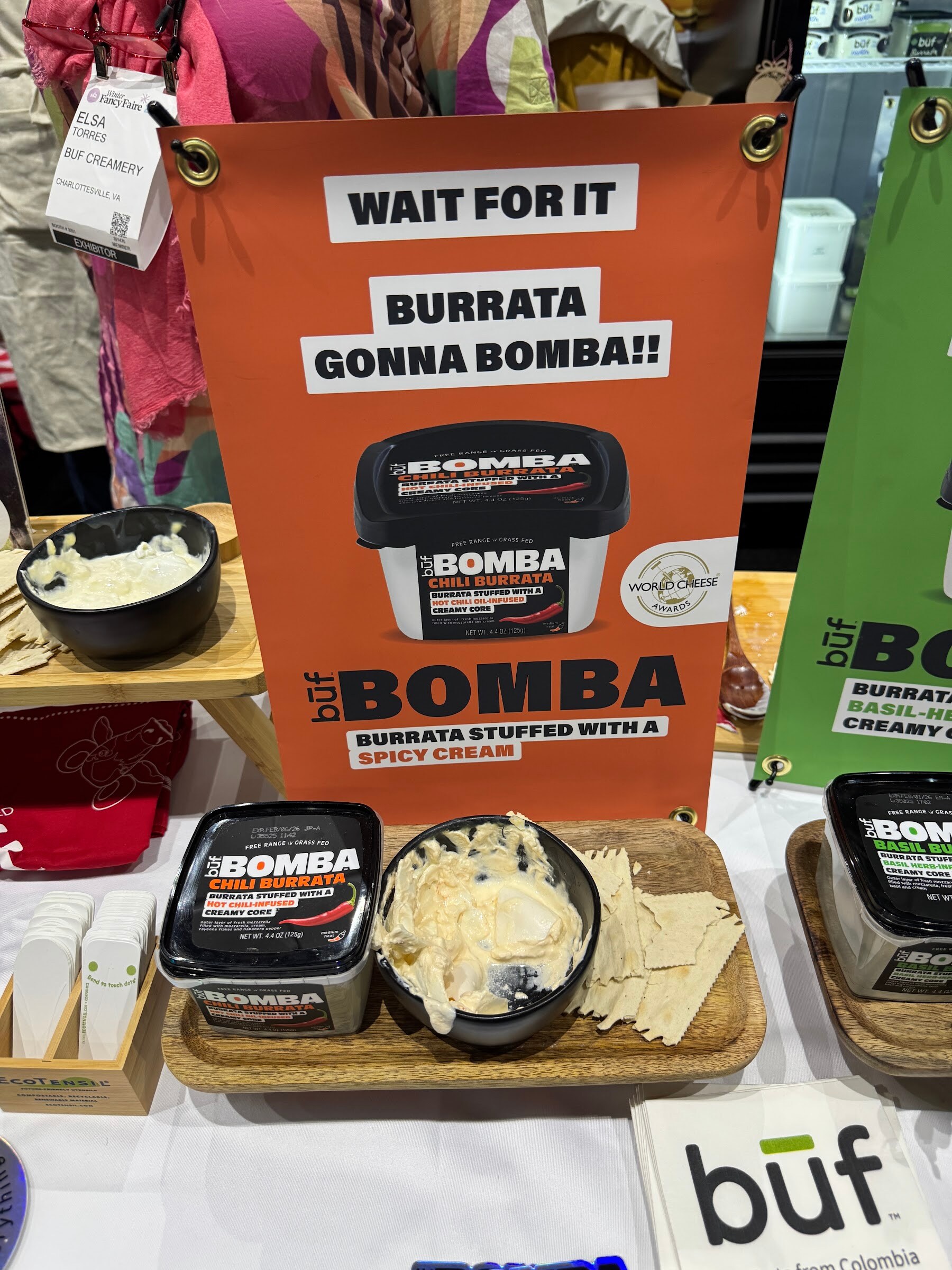 Tubs of büf Bomba burrata and a bowl of burrata under an orange sign reading Wait for it, Burrata Gonna Bomba.