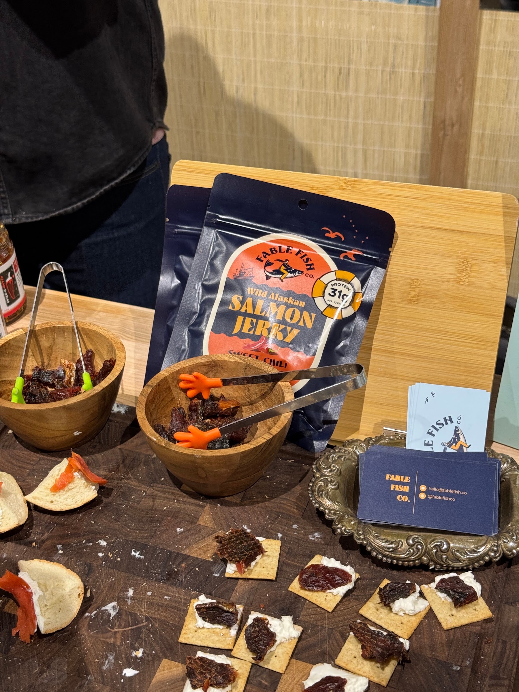Bag of Fable Fish Co. salmon jerky with bowls of jerky and crackers topped with jerky and cream cheese.
