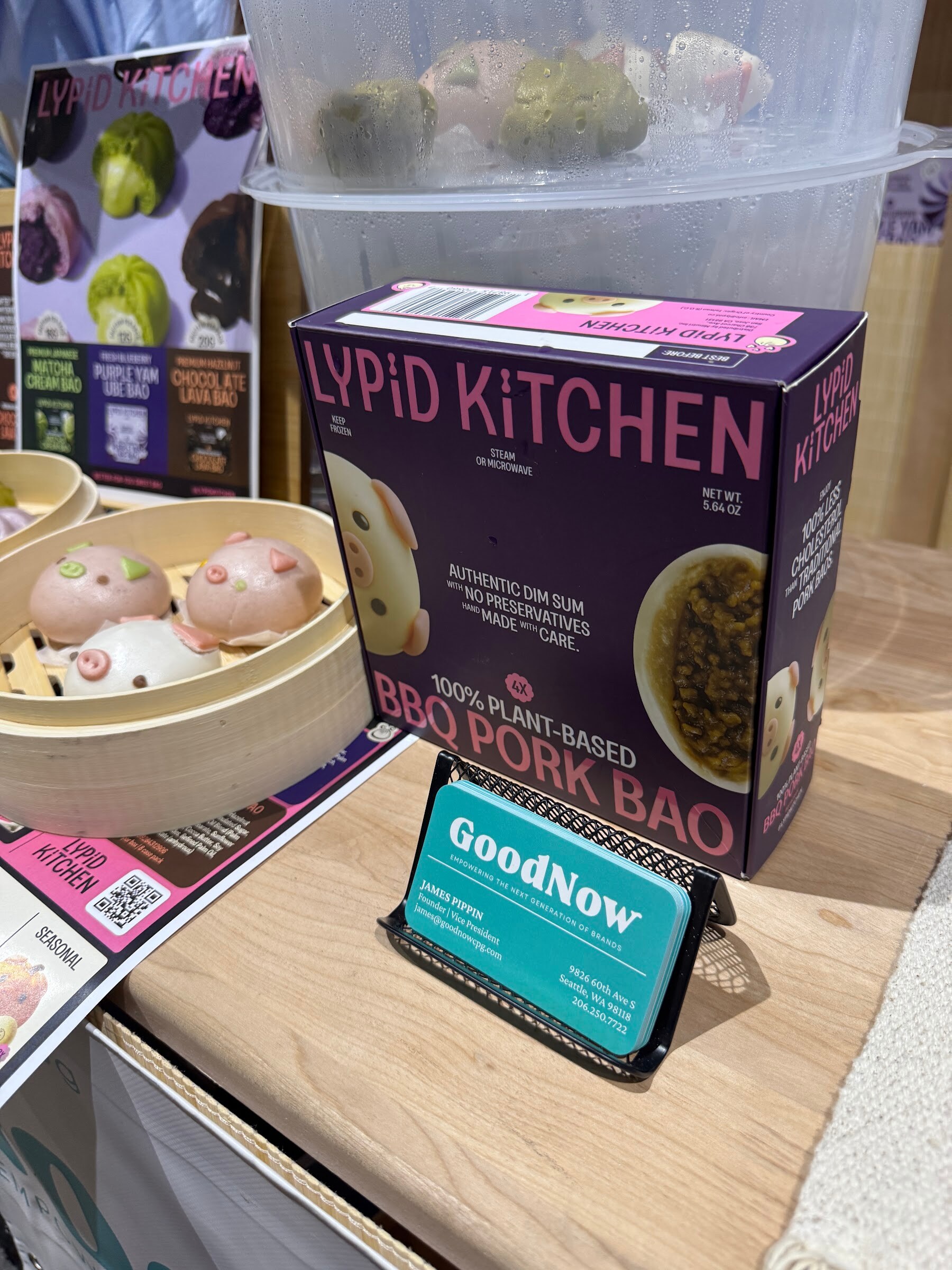 A Lypid Kitchen BBQ pork bao box beside a bamboo steamer of buns.