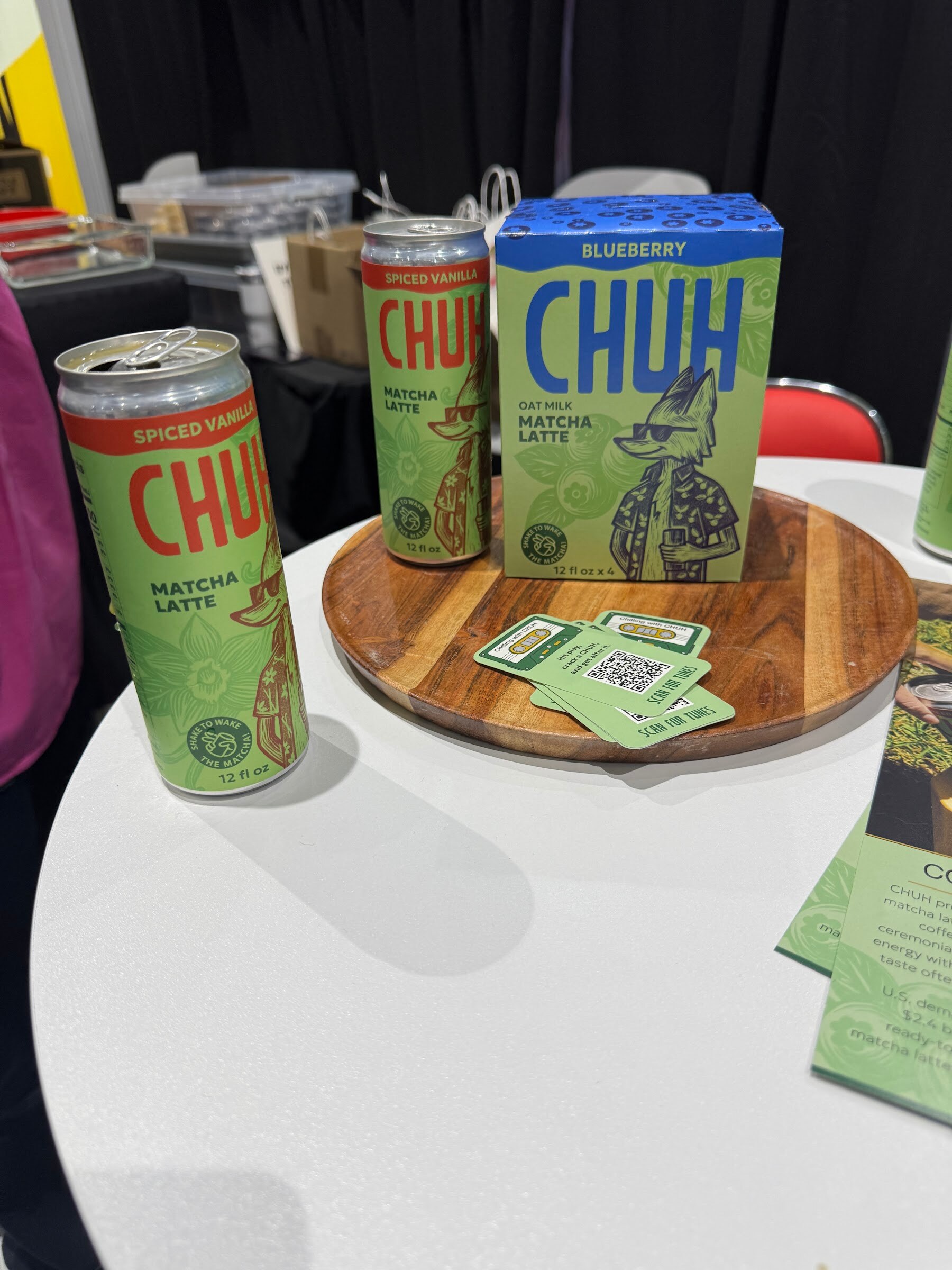 Green matcha latte cans and a box on a round wooden tray on a white table.