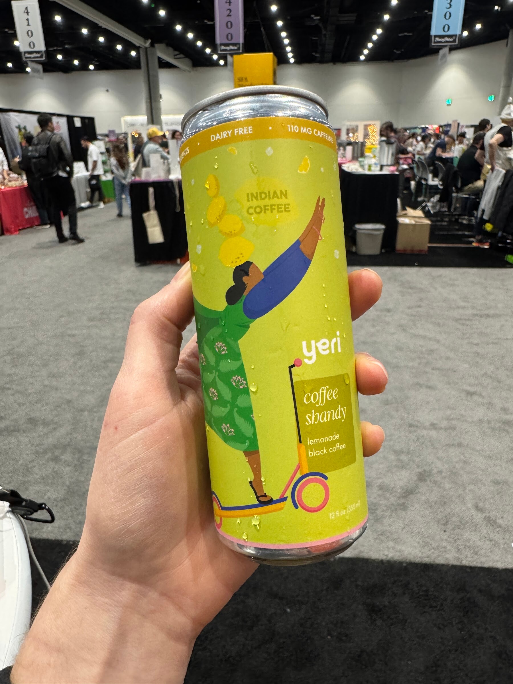 Hand holds a yellow-green can of yeri coffee shandy above the show floor.