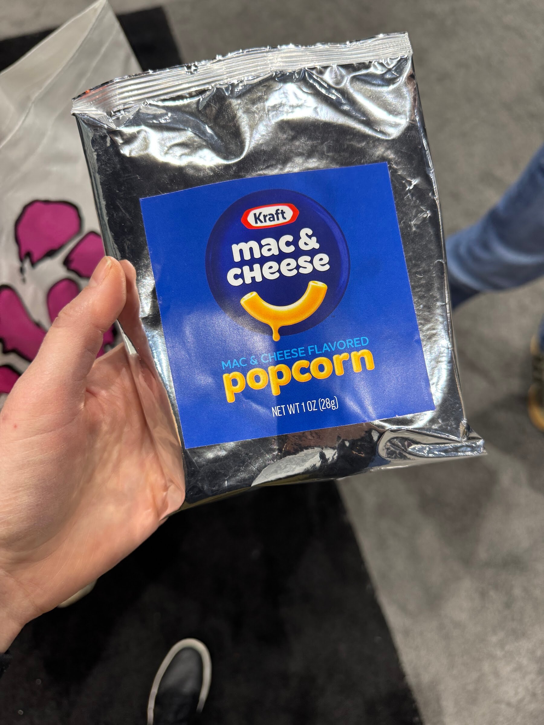 Hand holds a foil bag of Kraft mac & cheese flavored popcorn.