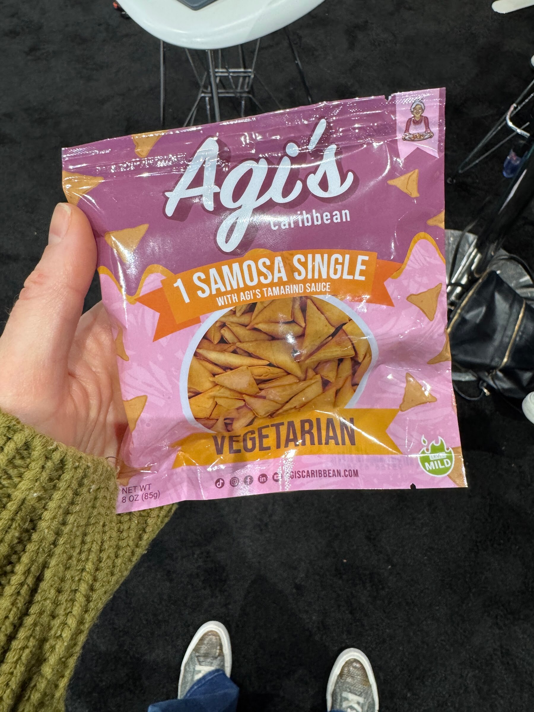 Hand holds a pink pouch of Agi’s Caribbean samosa single, vegetarian.