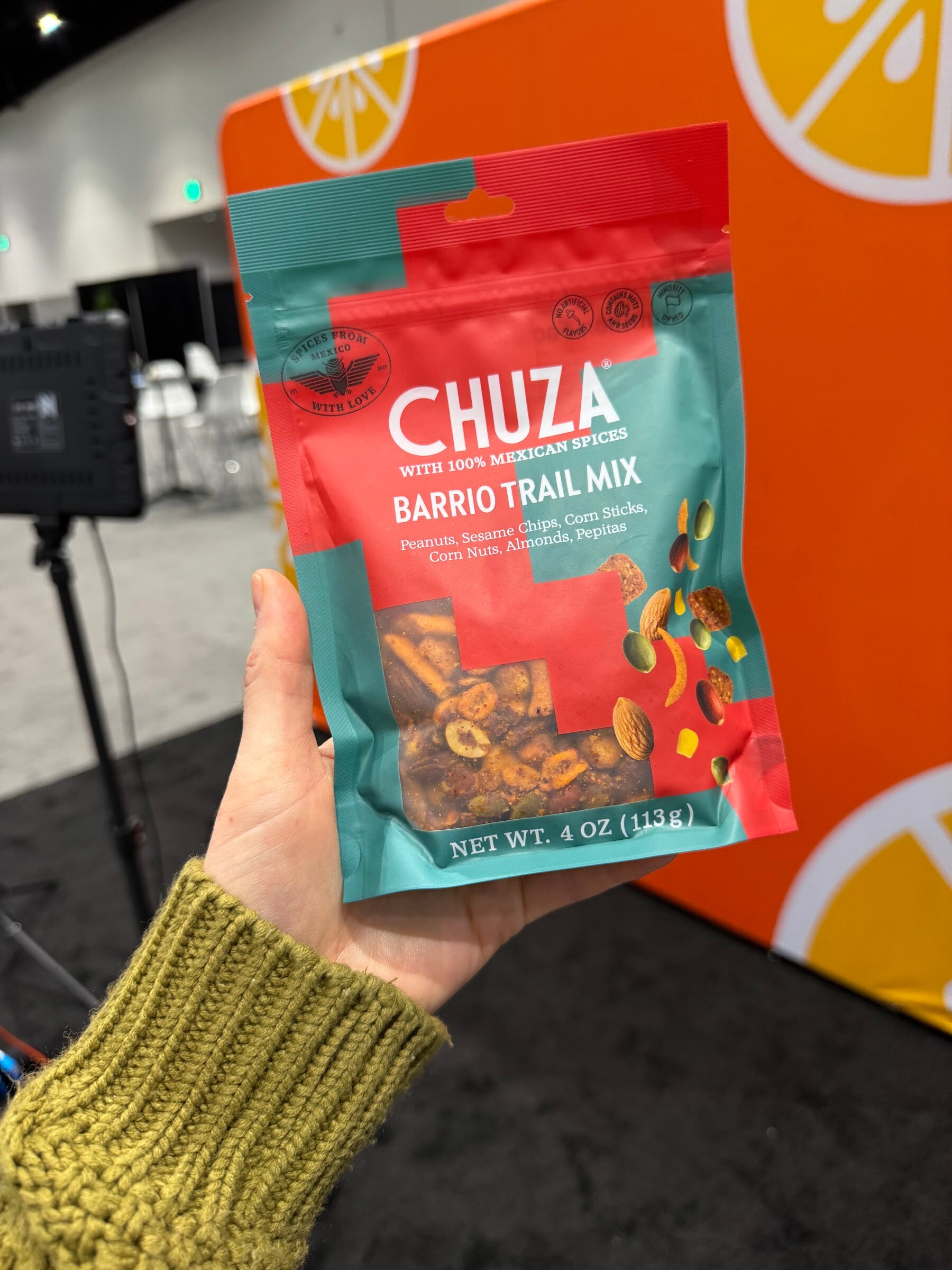Hand holds a bag of Chuza Barrio Trail Mix in front of the orange Taste Radio backdrop.