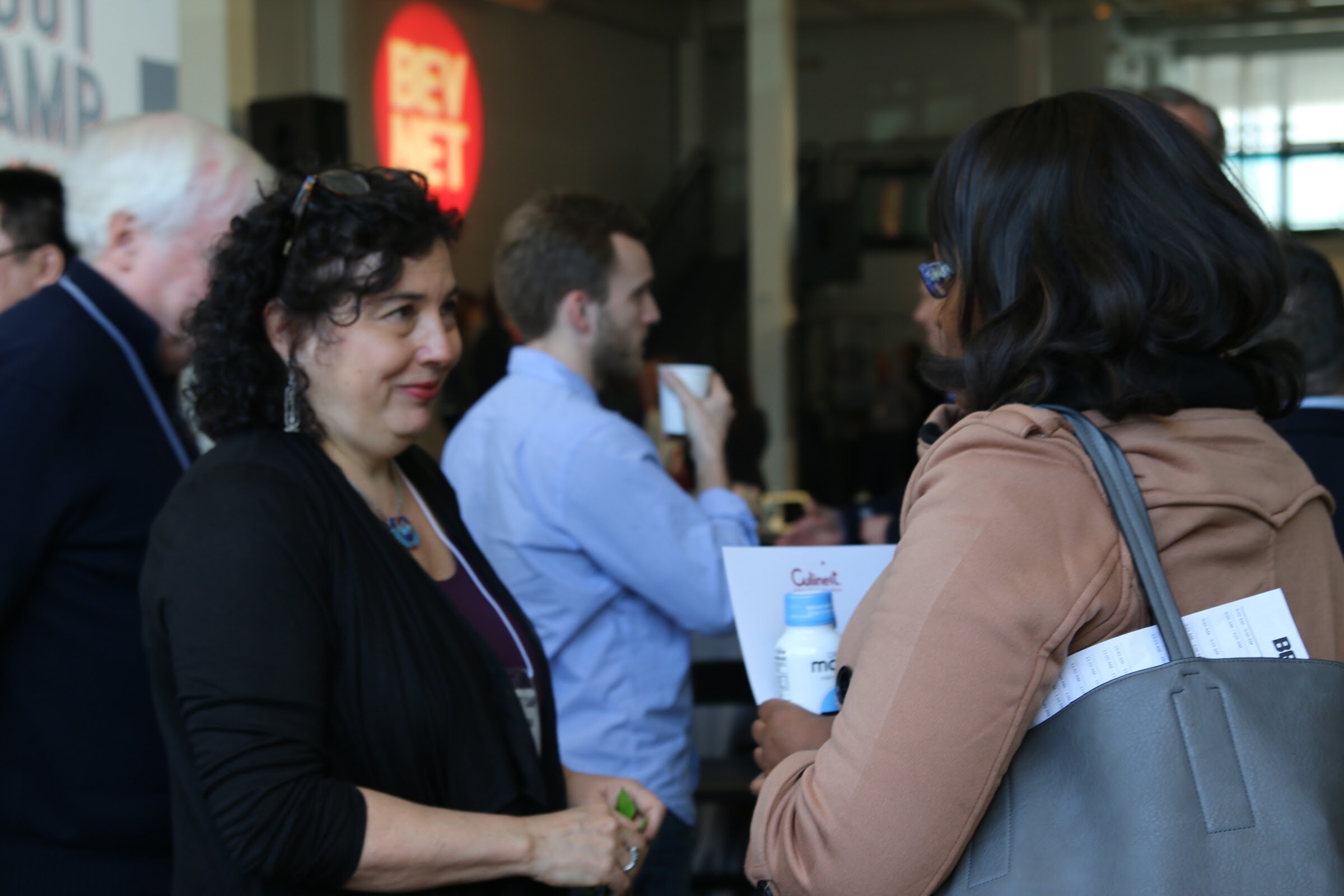 Attendees talk in front of BevNET logo, Culinet folder with Maple bottle in hand.