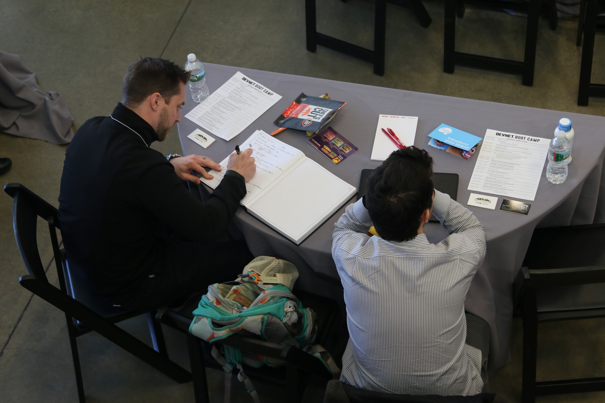 Overhead of two attendees at table taking notes on BevNET Boot Camp agenda sheets.