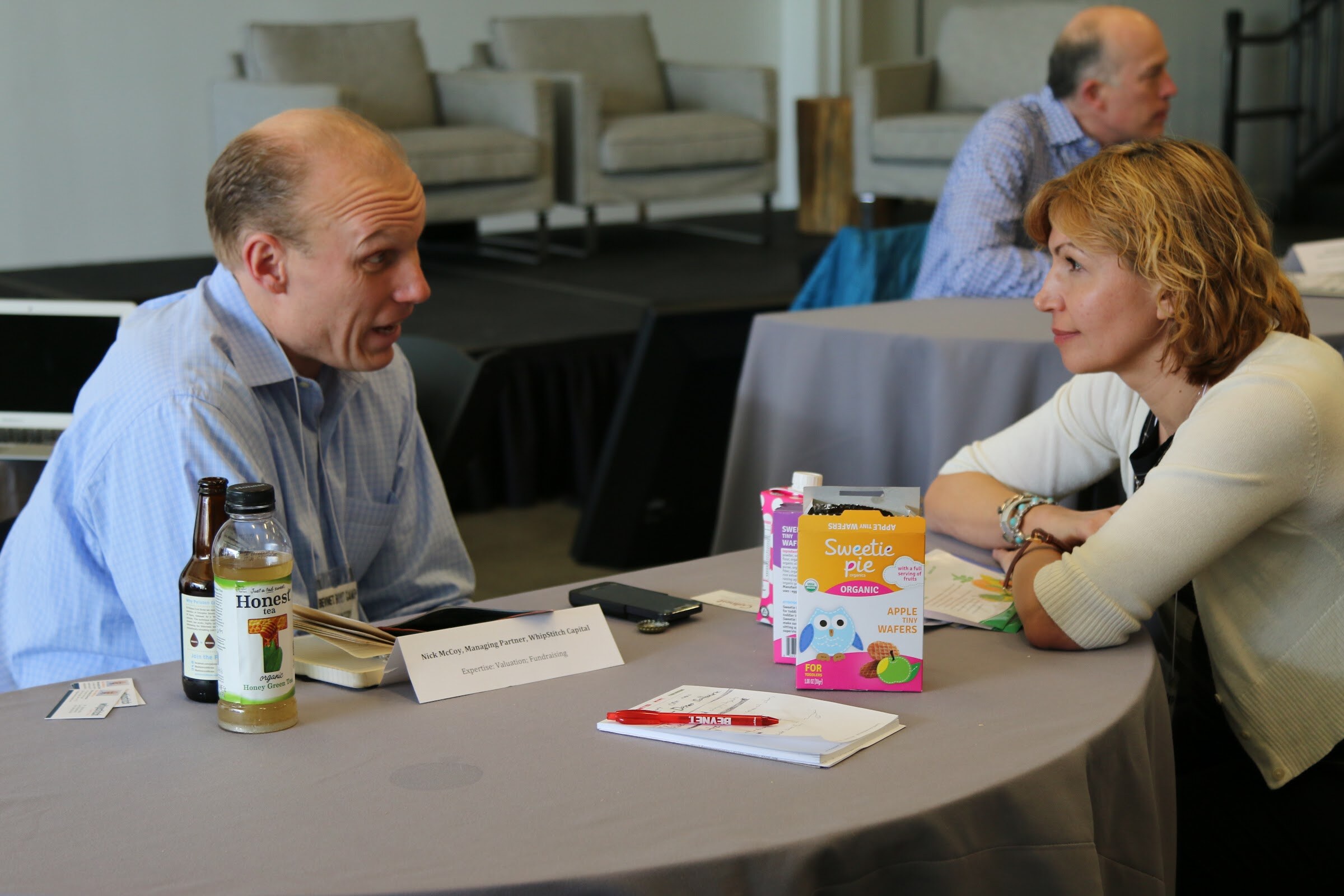 Two attendees in meeting, Honest Tea and Sweetie Pie wafers box on table, name placard.