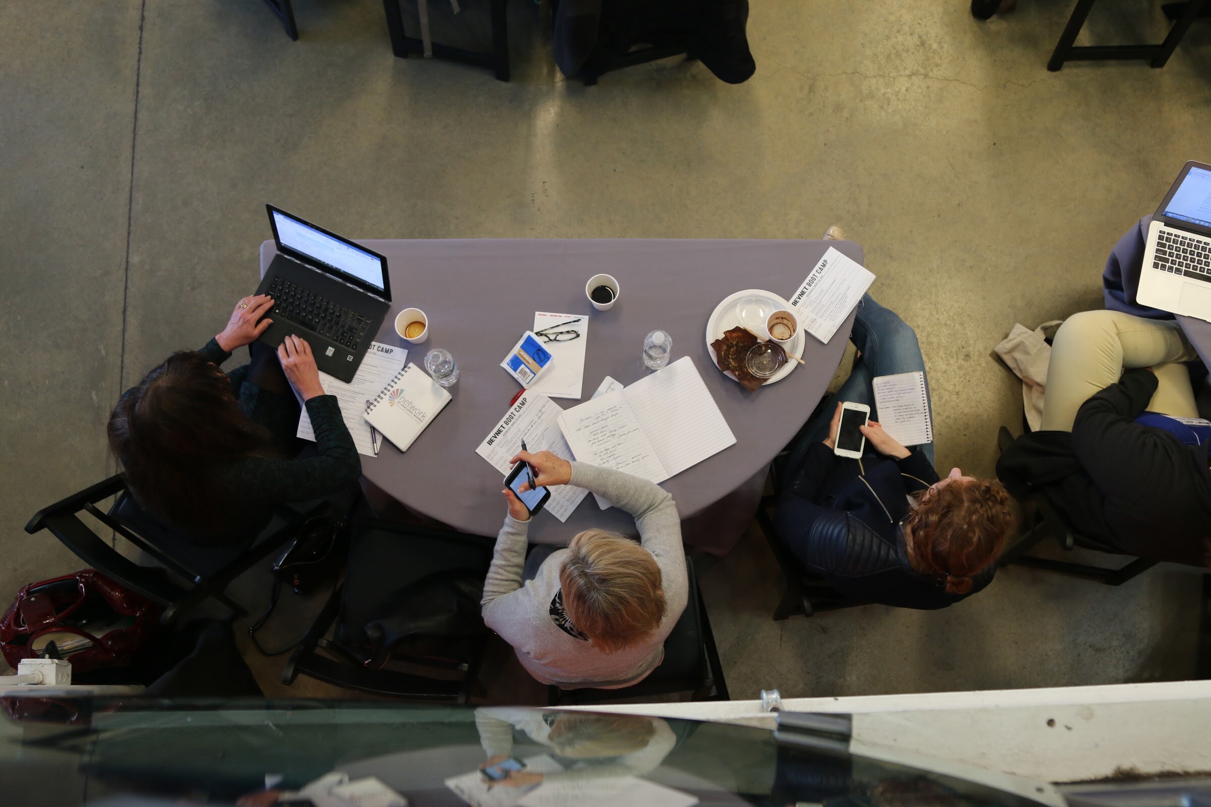 Overhead view of a table with a laptop, notebooks, phones and coffee cups at BevNET Boot Camp.