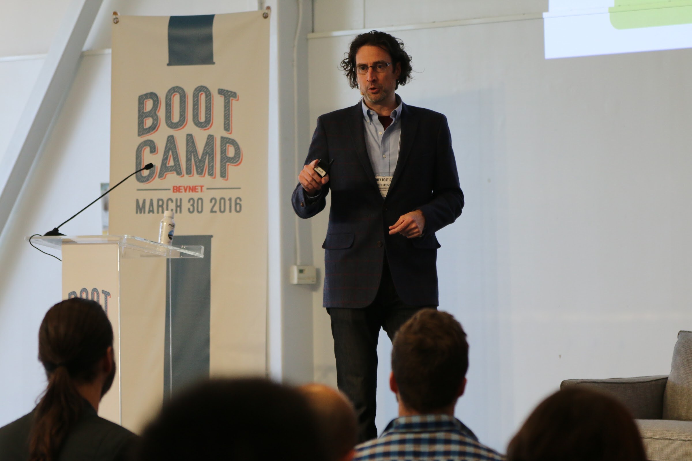 Presenter at Boot Camp banner, audience heads in foreground.