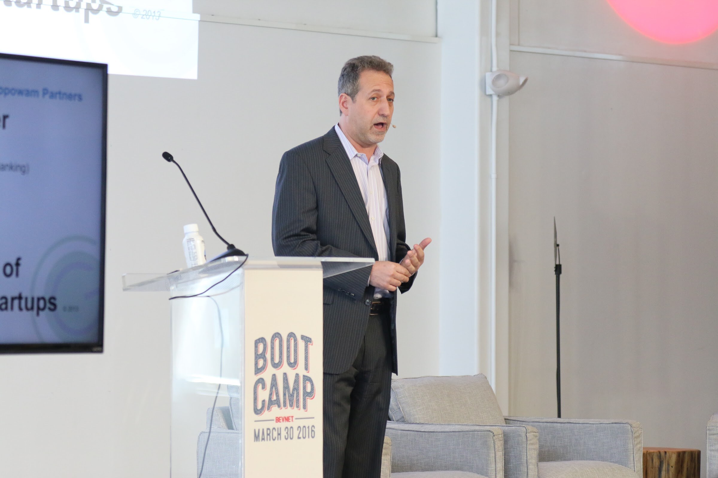 Presenter at Boot Camp podium, monitor shows Raising Capital for Startups.