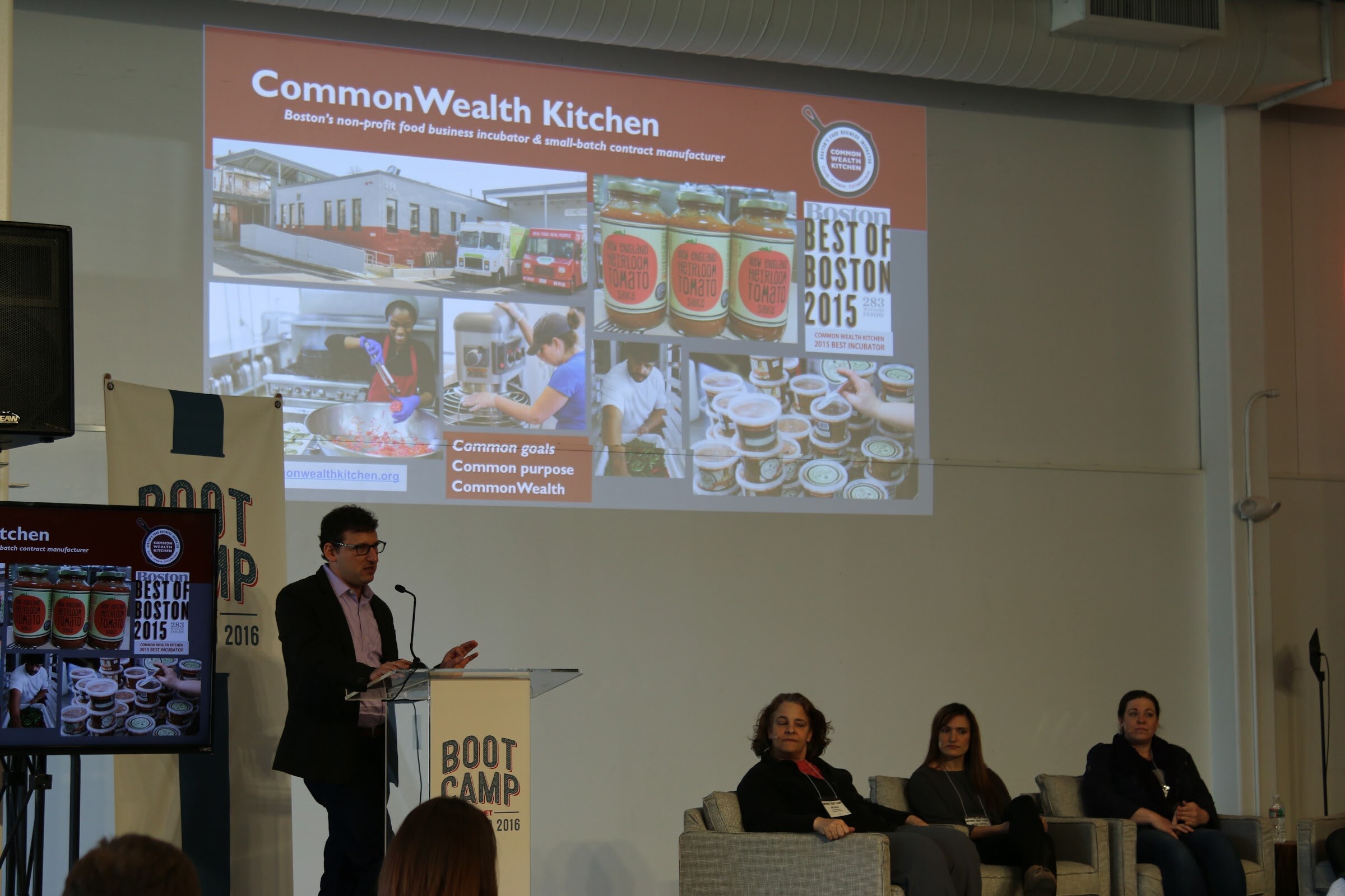 Presenter at podium, slide CommonWealth Kitchen, three panelists seated in armchairs.