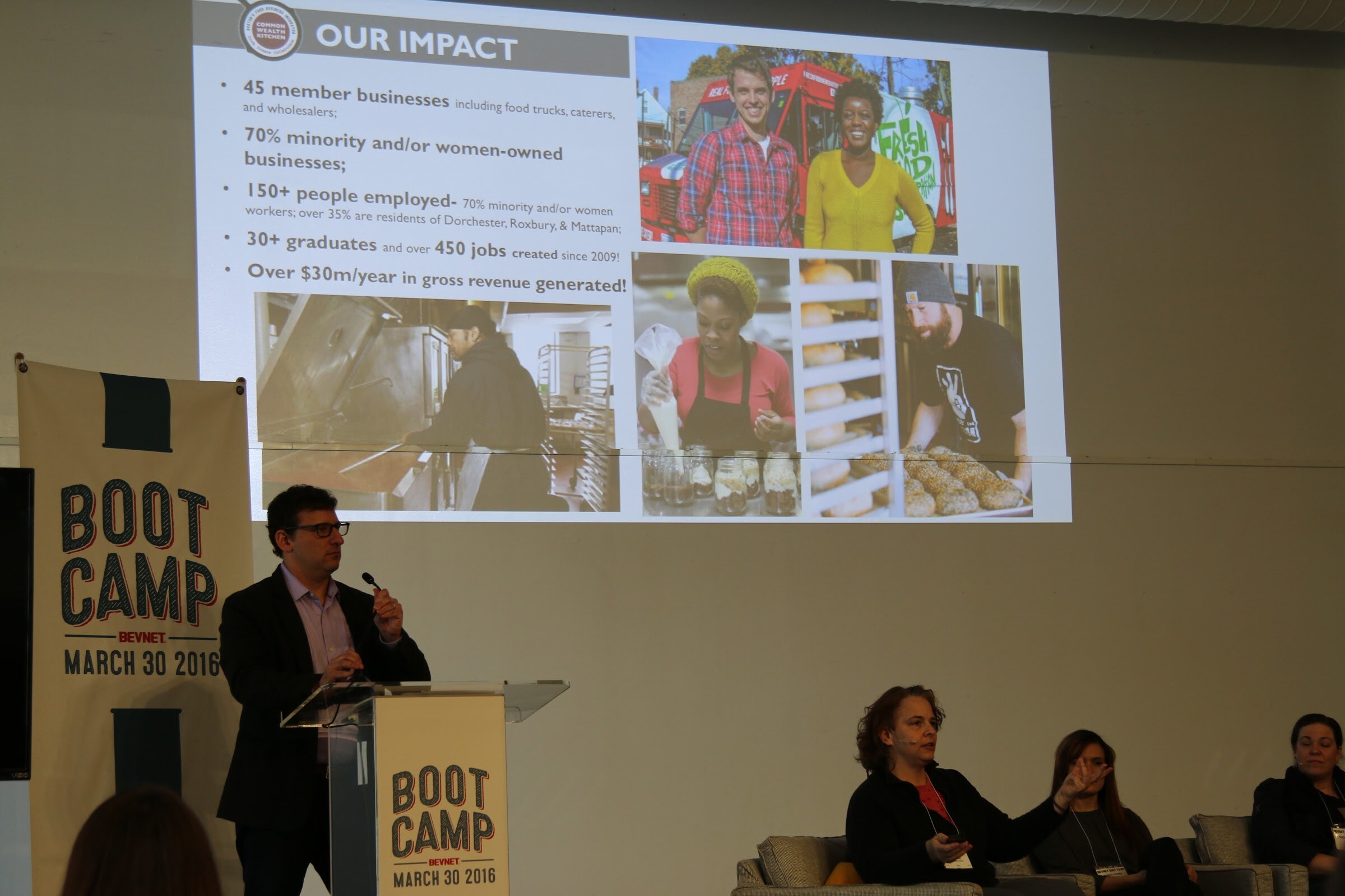 Presenter at podium, slide Our Impact (CommonWealth Kitchen branding) member businesses; panelists seated at right, one gesturing.