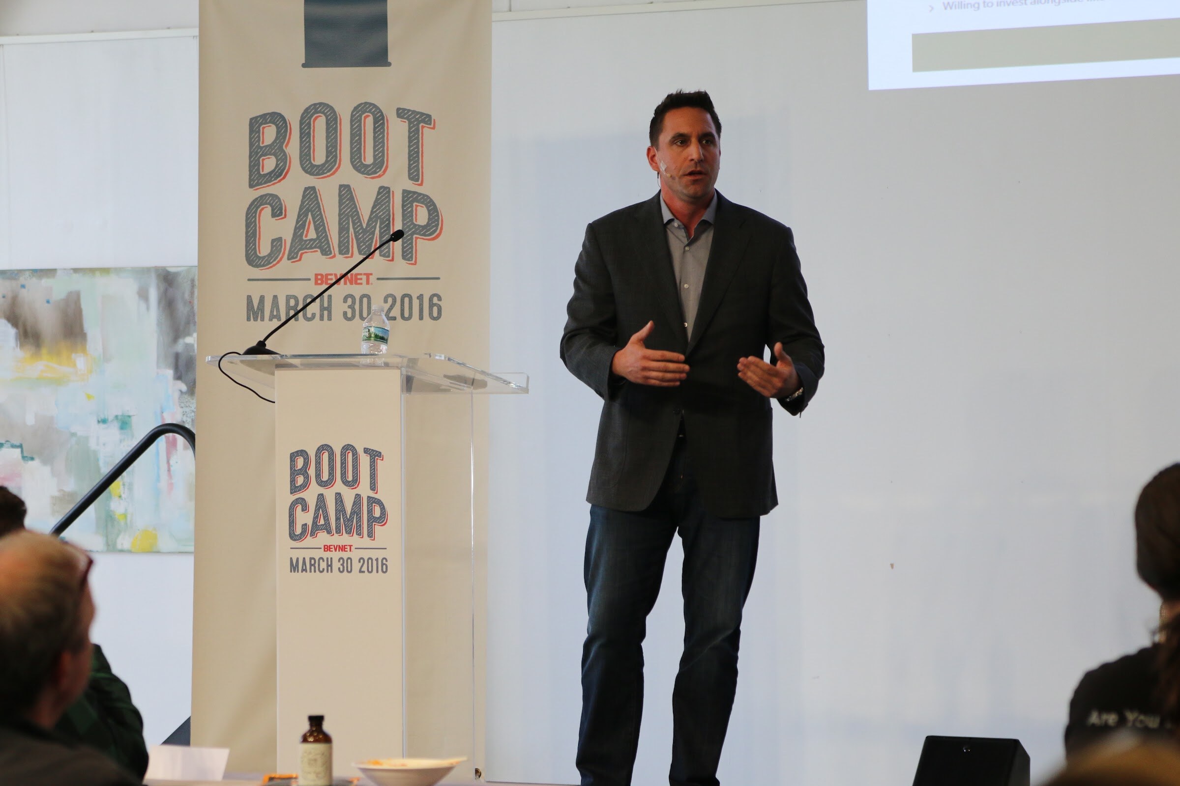 Presenter gesturing, Boot Camp banner and podium, audience heads foreground.