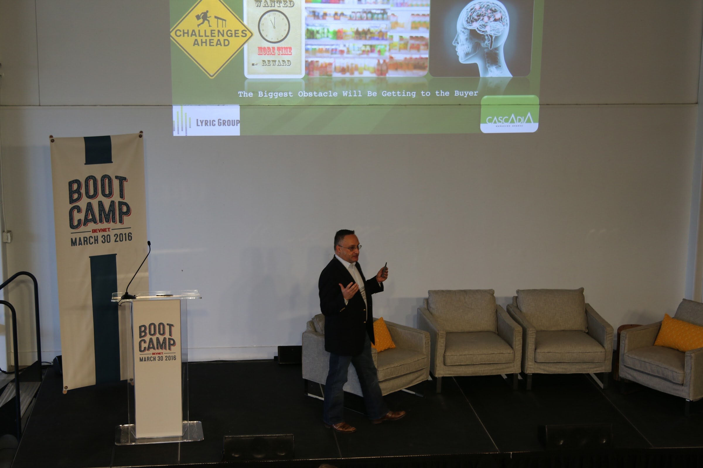 Presenter walking on stage, slide Challenges Ahead The Biggest Obstacle Will Be Getting to the Buyer (Lyric Group, Cascadia logos).