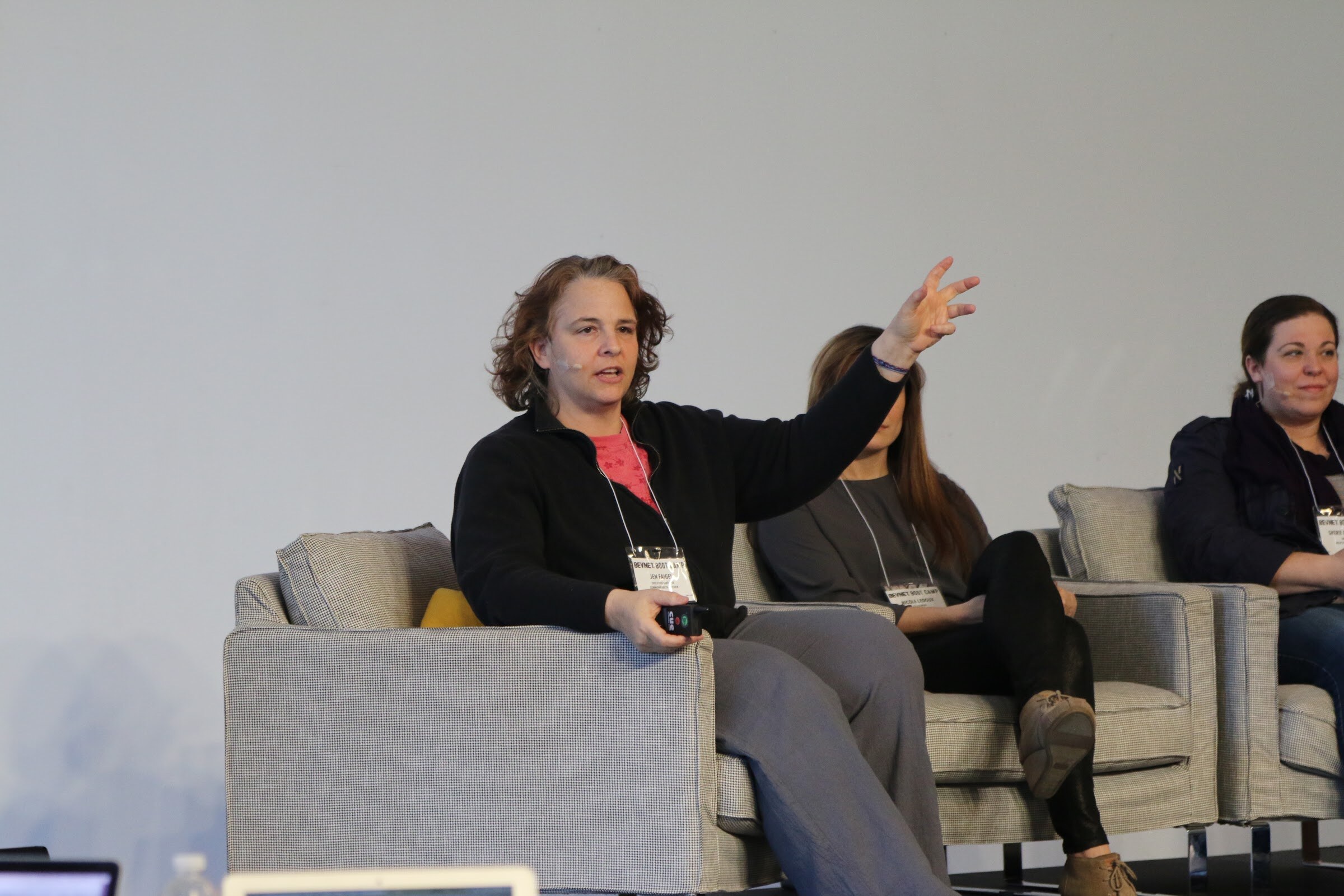 Seated panelist gestures with raised arm, two other panelists beside her.