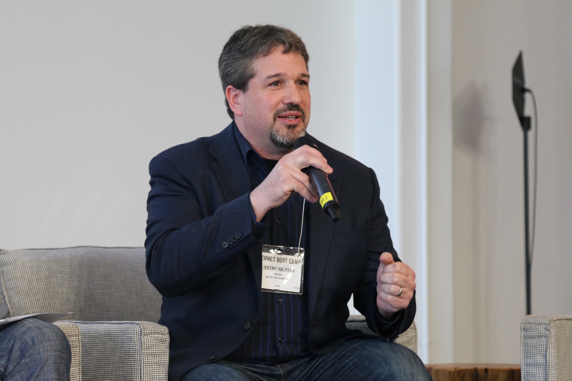 Seated panelist speaks into handheld microphone, close.