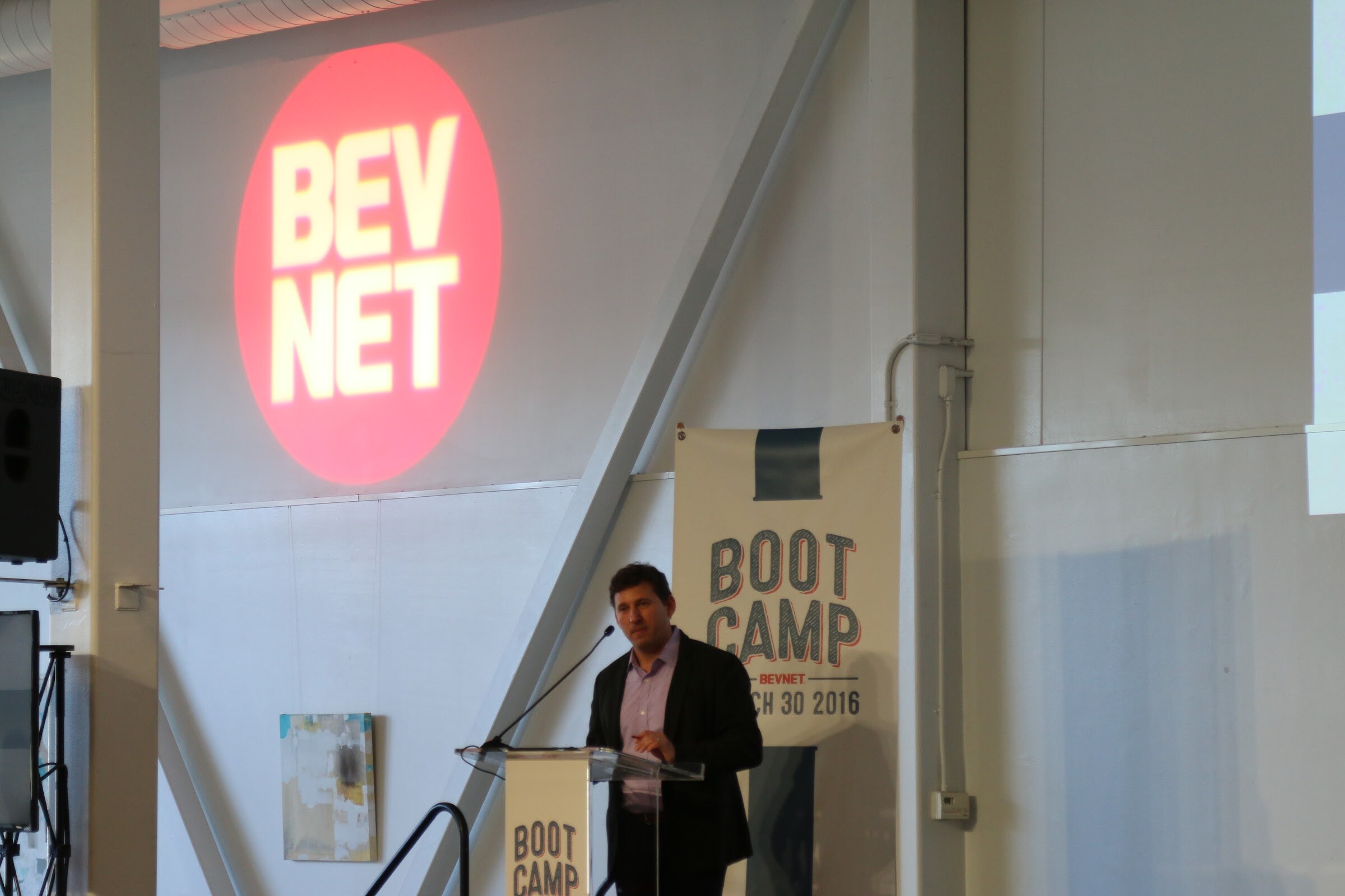 Speaker at podium BevNET red logo projection on wall, Boot Camp banner.