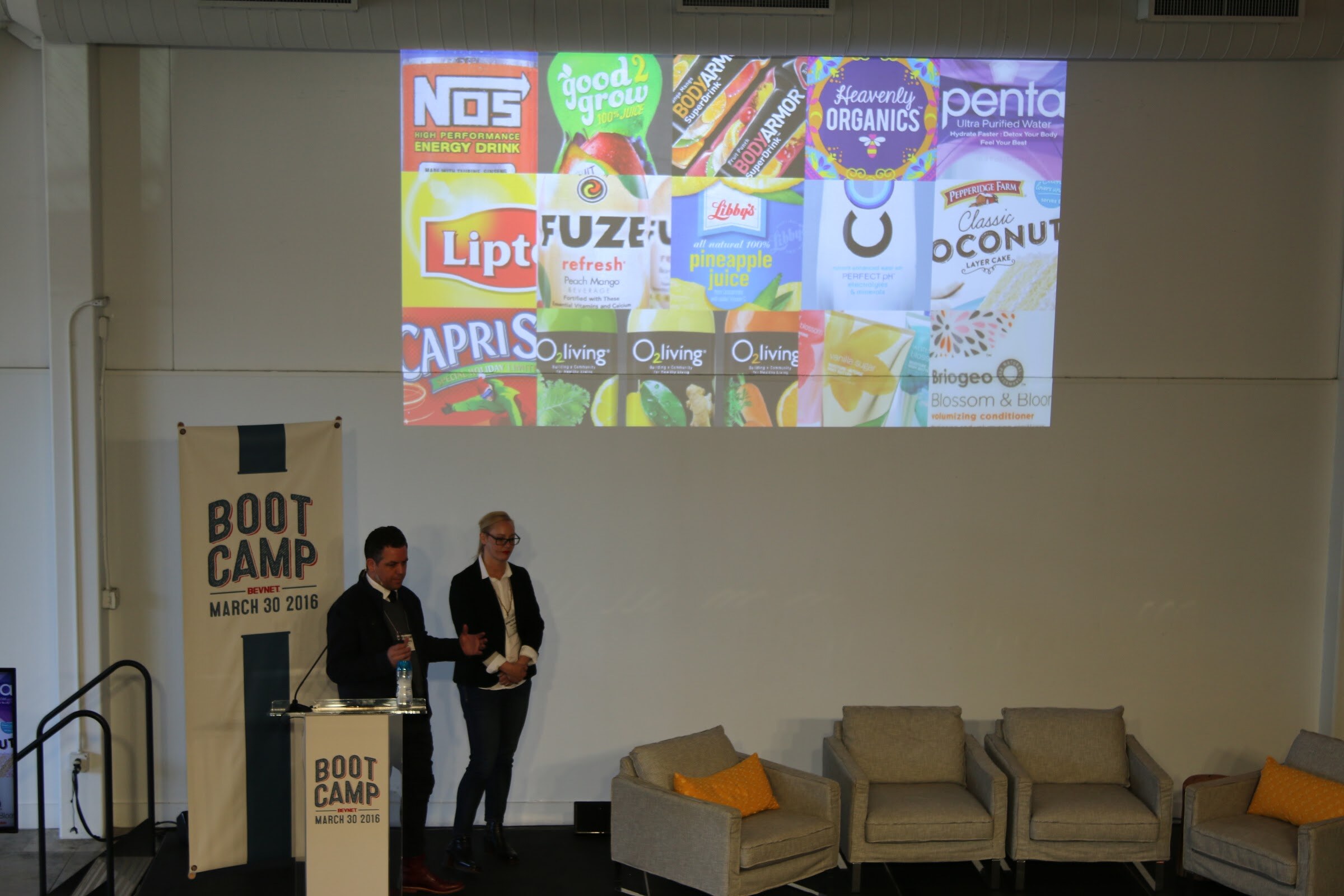 Two presenters on stage, projected montage of beverage and food brand labels (NOS, Lipton, Fuze, Capri, Penta, Heavenly Organics...).