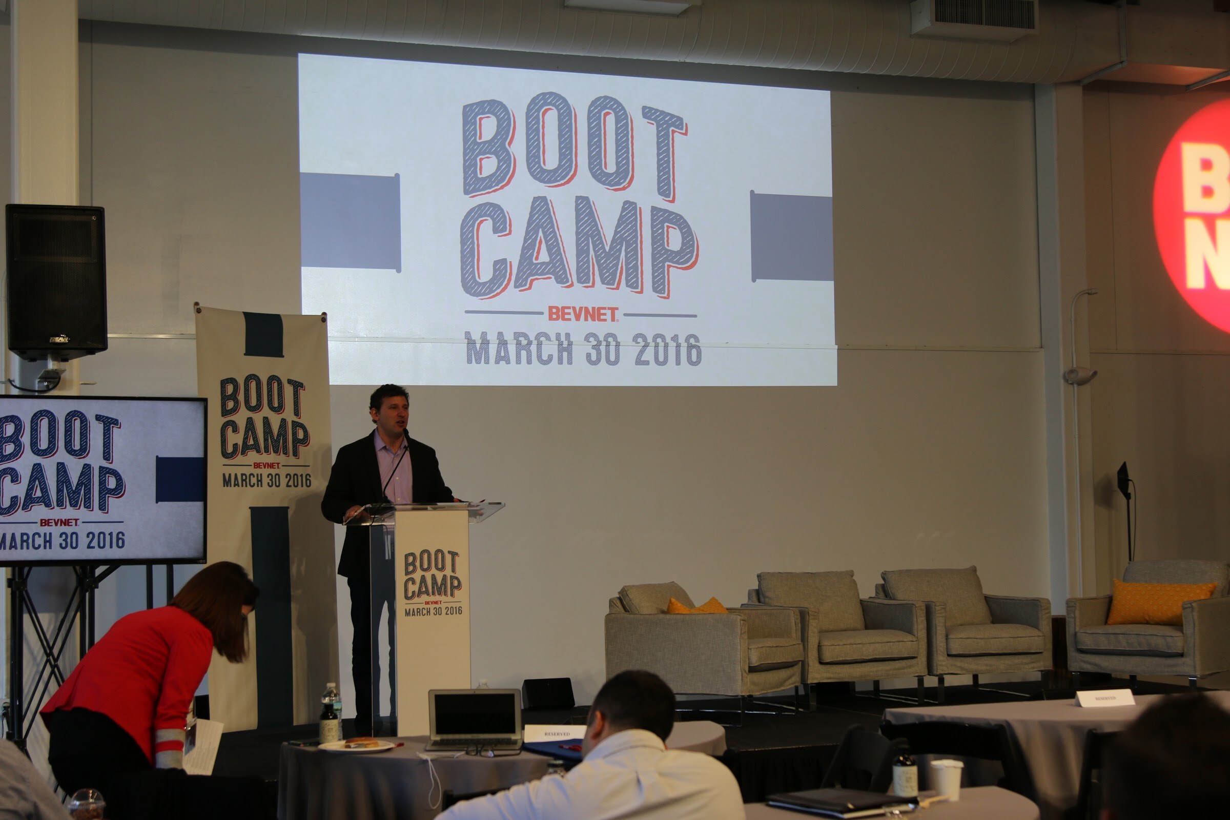 Wide stage: speaker at podium under Boot Camp slide, BevNET logo projected on wall; audience tables foreground.