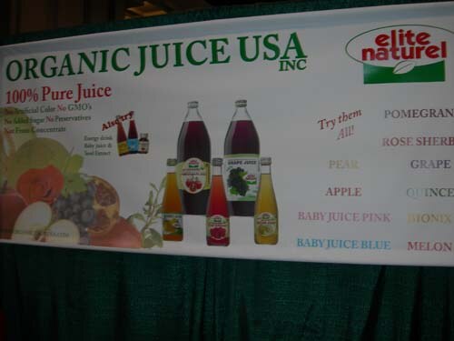 A banner reading Organic Juice USA Inc, 100% Pure Juice, with the Elite Naturel logo, showing bottles of juice and a list of flavors including pomegranate, pear, apple and grape.