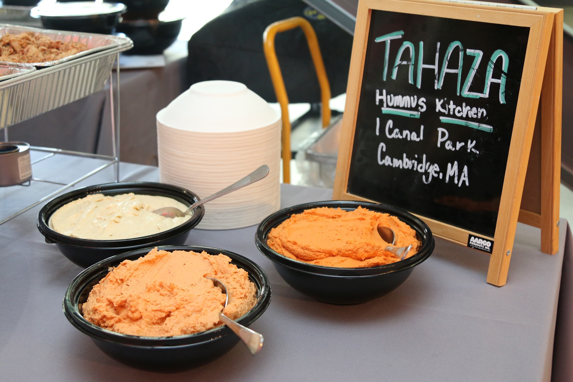 Bowls of hummus beside chalkboard sign Tahaza Hummus Kitchen, 1 Canal Park Cambridge MA.