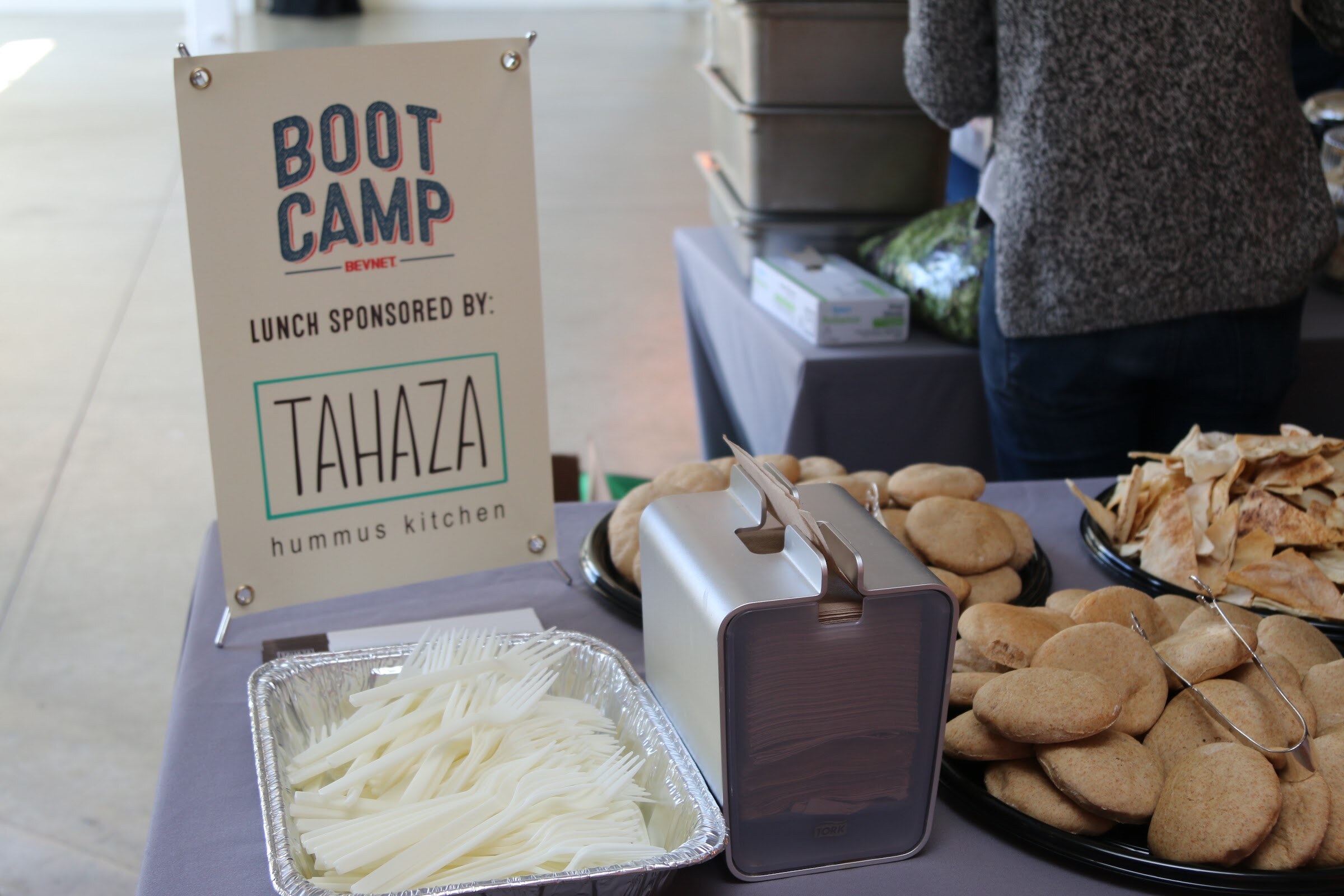 Sign Boot Camp BevNET Lunch sponsored by Tahaza hummus kitchen, pita bread, tray of forks.