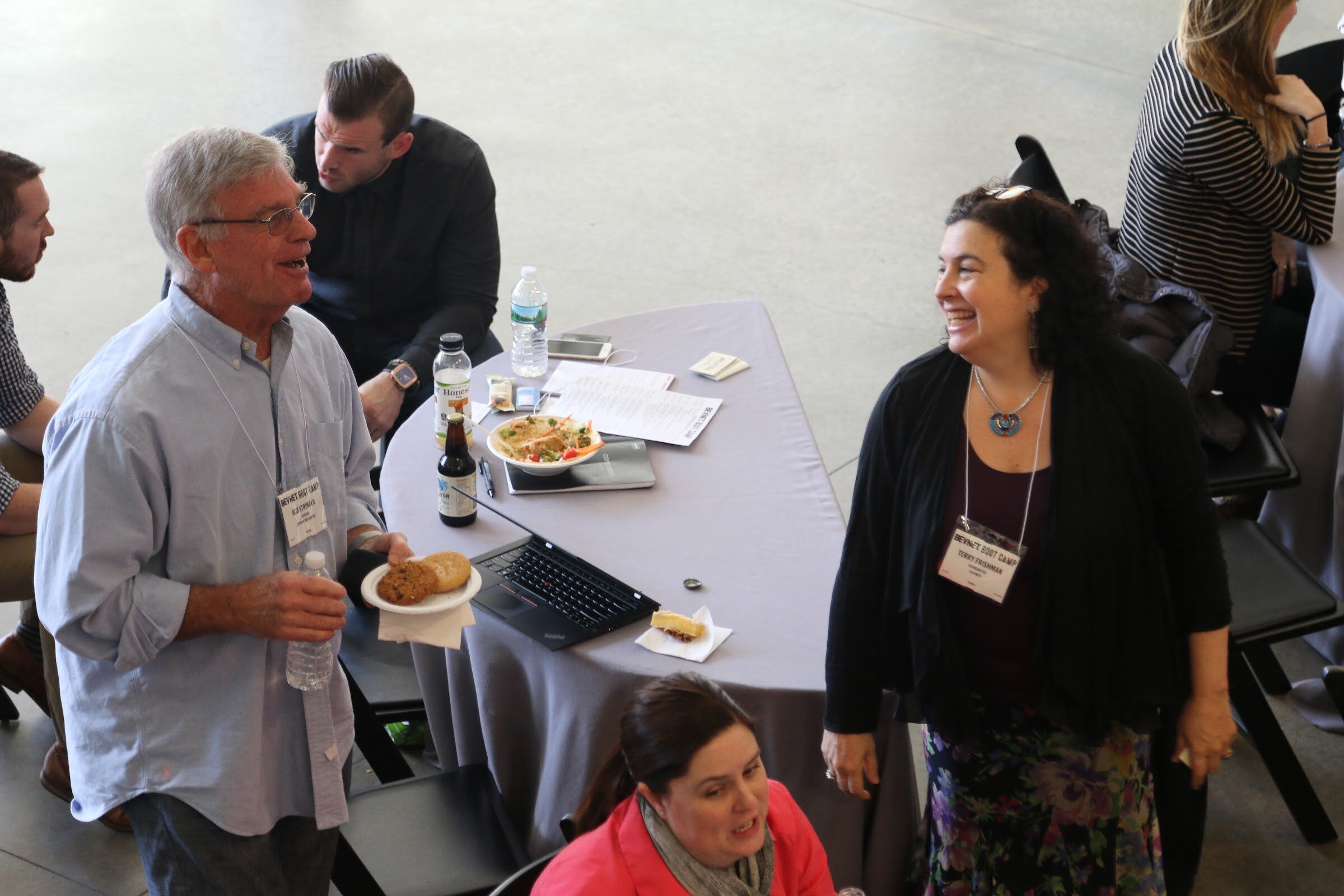 Overhead of attendees chatting beside lunch table, man with cookie plate and woman laughing.