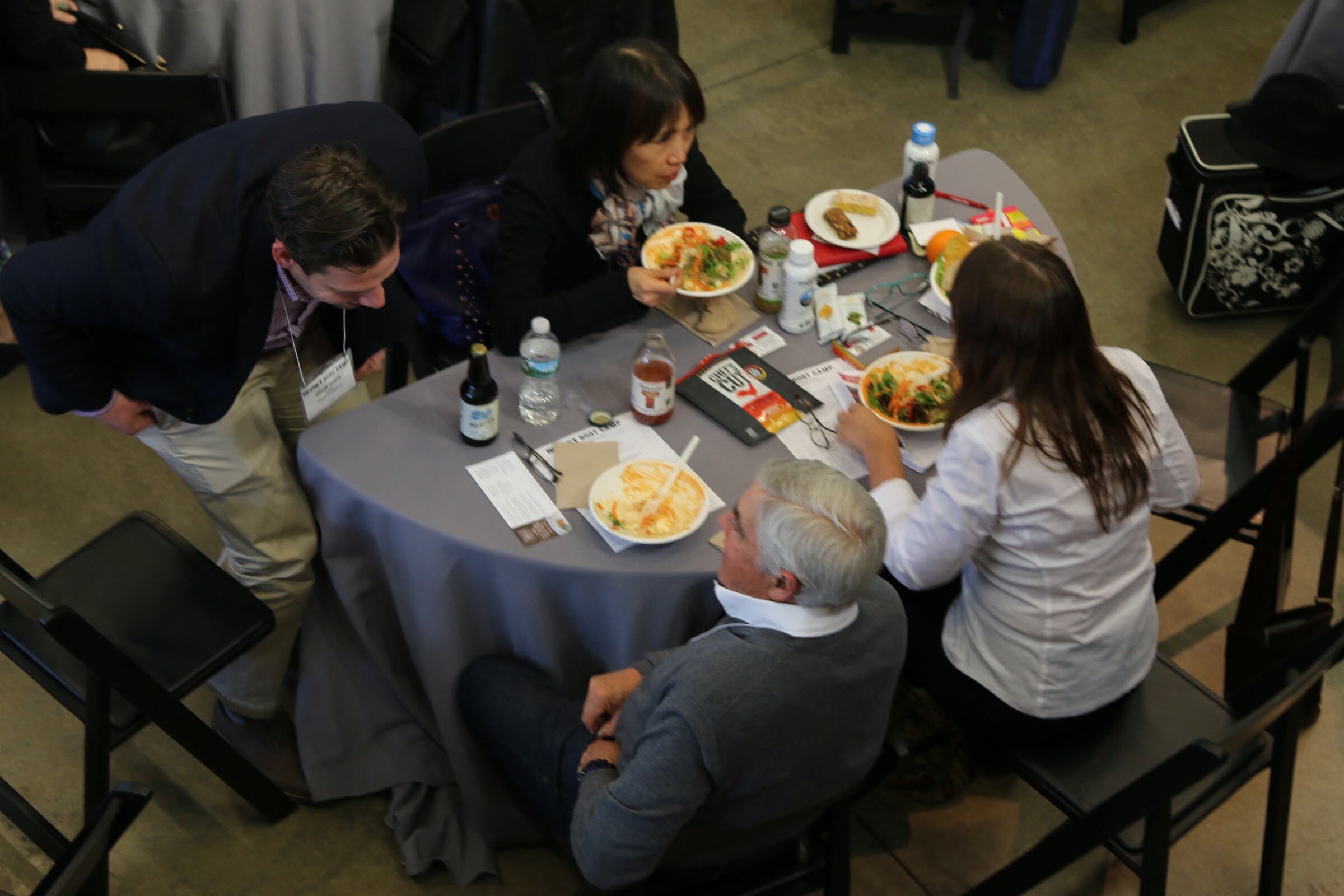 Overhead of lunch table: attendees eating salads and food on plates, drinks and flyers.