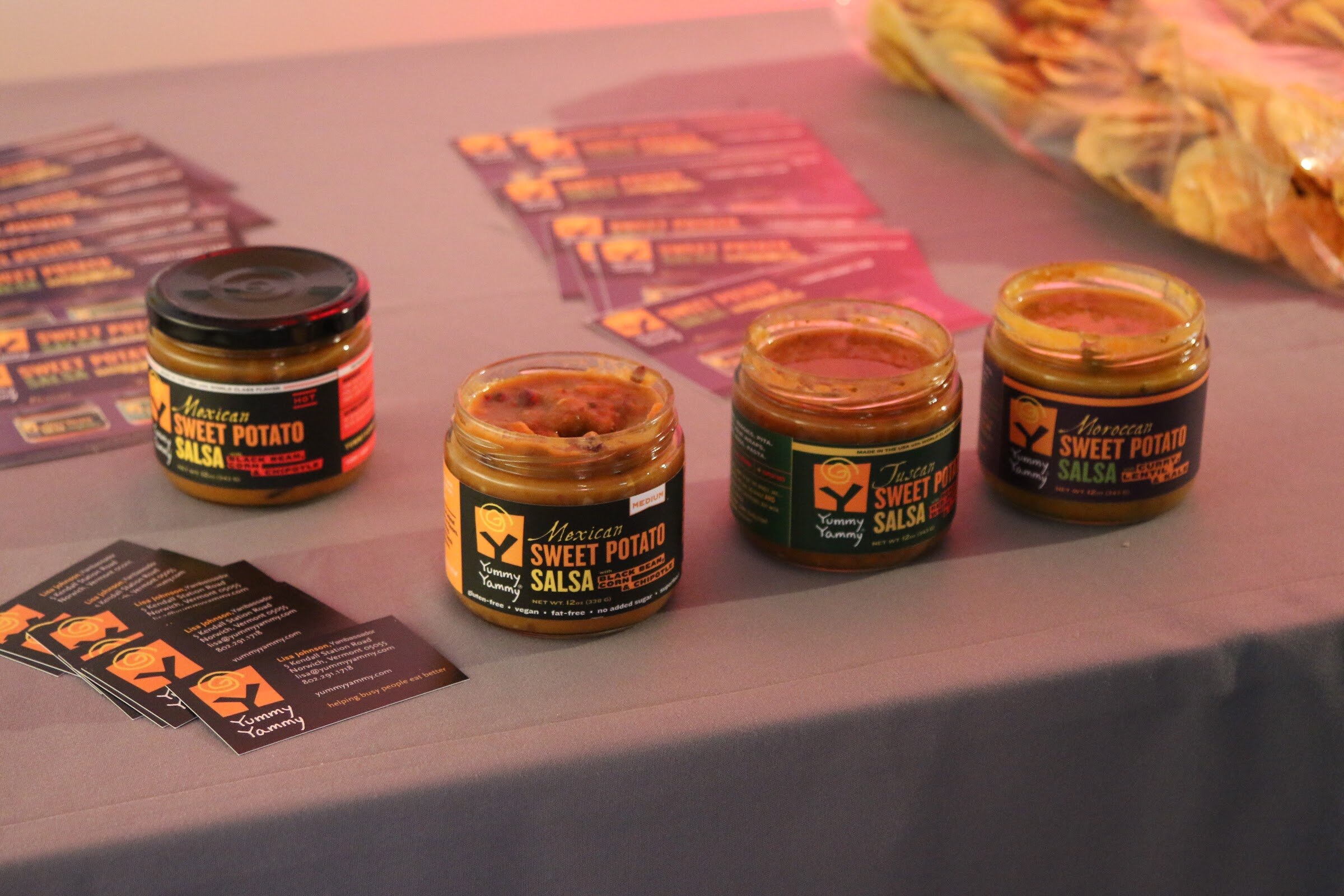 Four jars of Yummy Yammy sweet potato salsa (Mexican, Tuscan, Moroccan) on table with business cards.