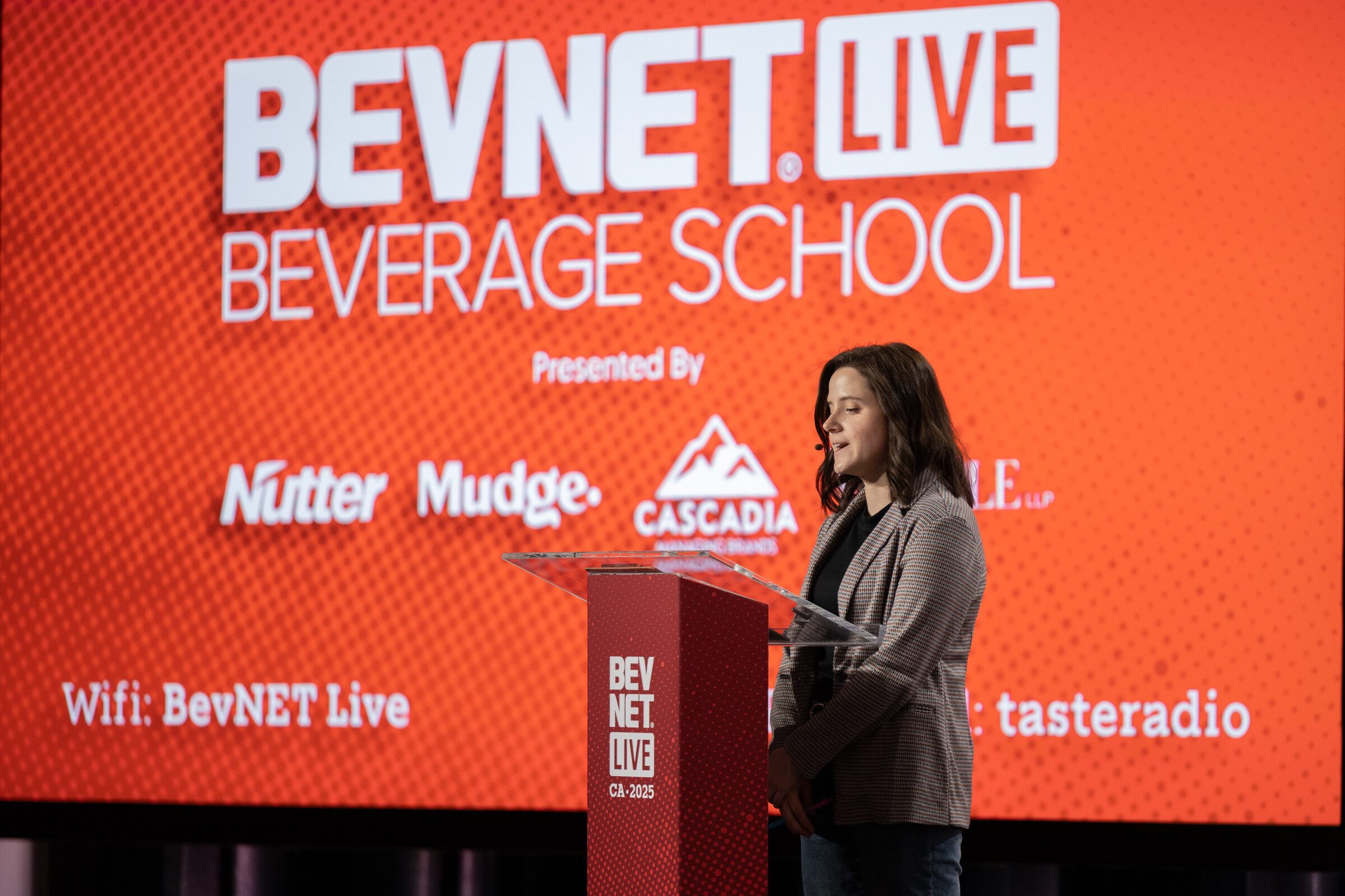 A woman speaks at a podium in front of a red BevNET Live Beverage School screen.