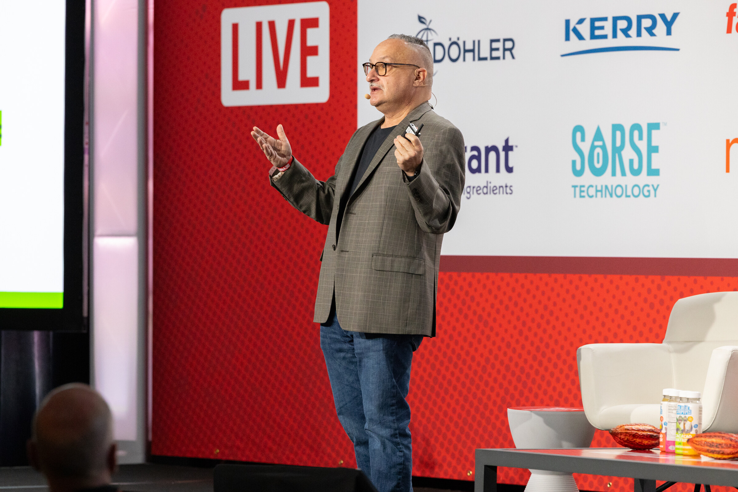 A man in a gray jacket speaks on stage in front of the BevNET Live backdrop.