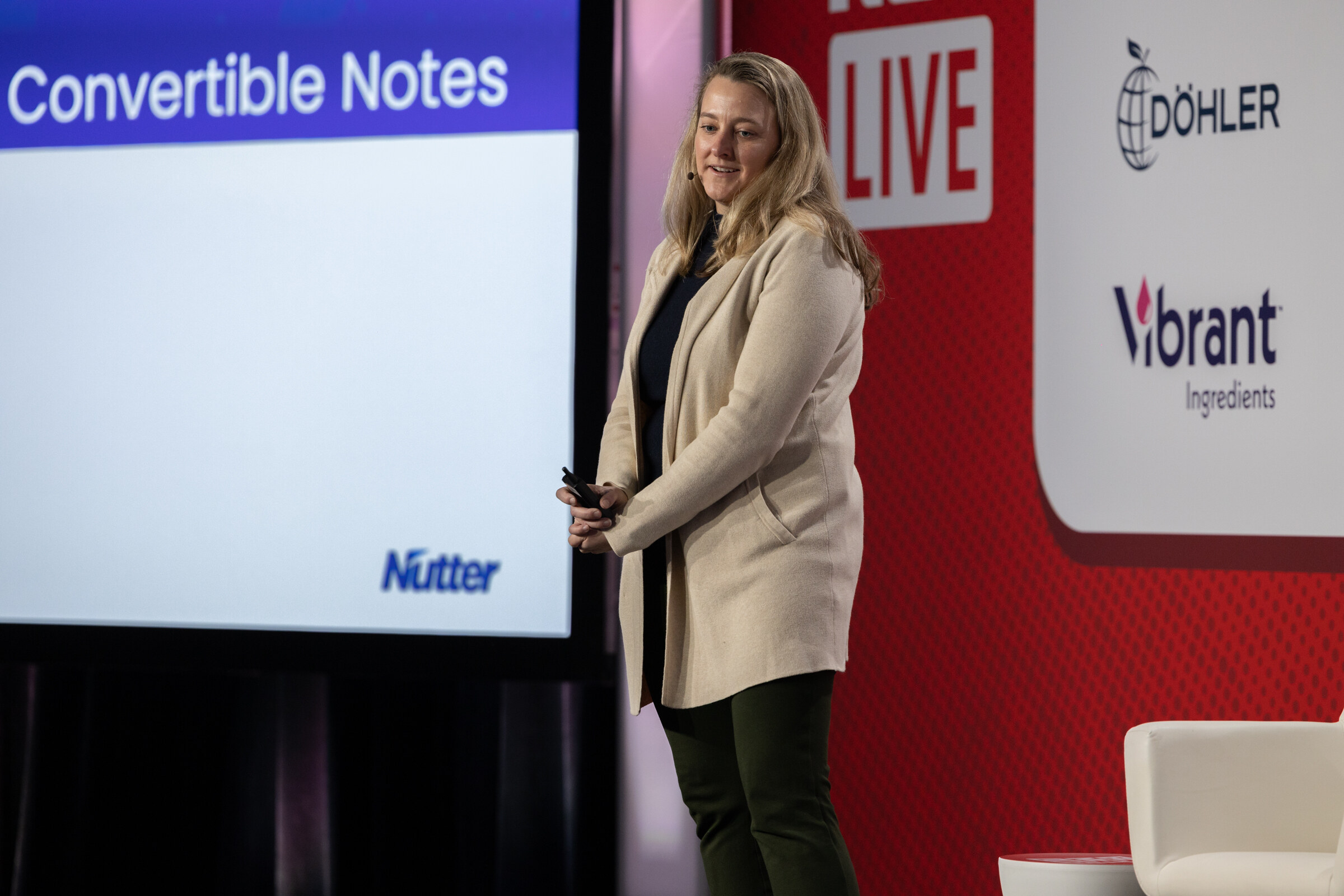 A woman in a cream blazer stands beside a slide titled Convertible Notes.