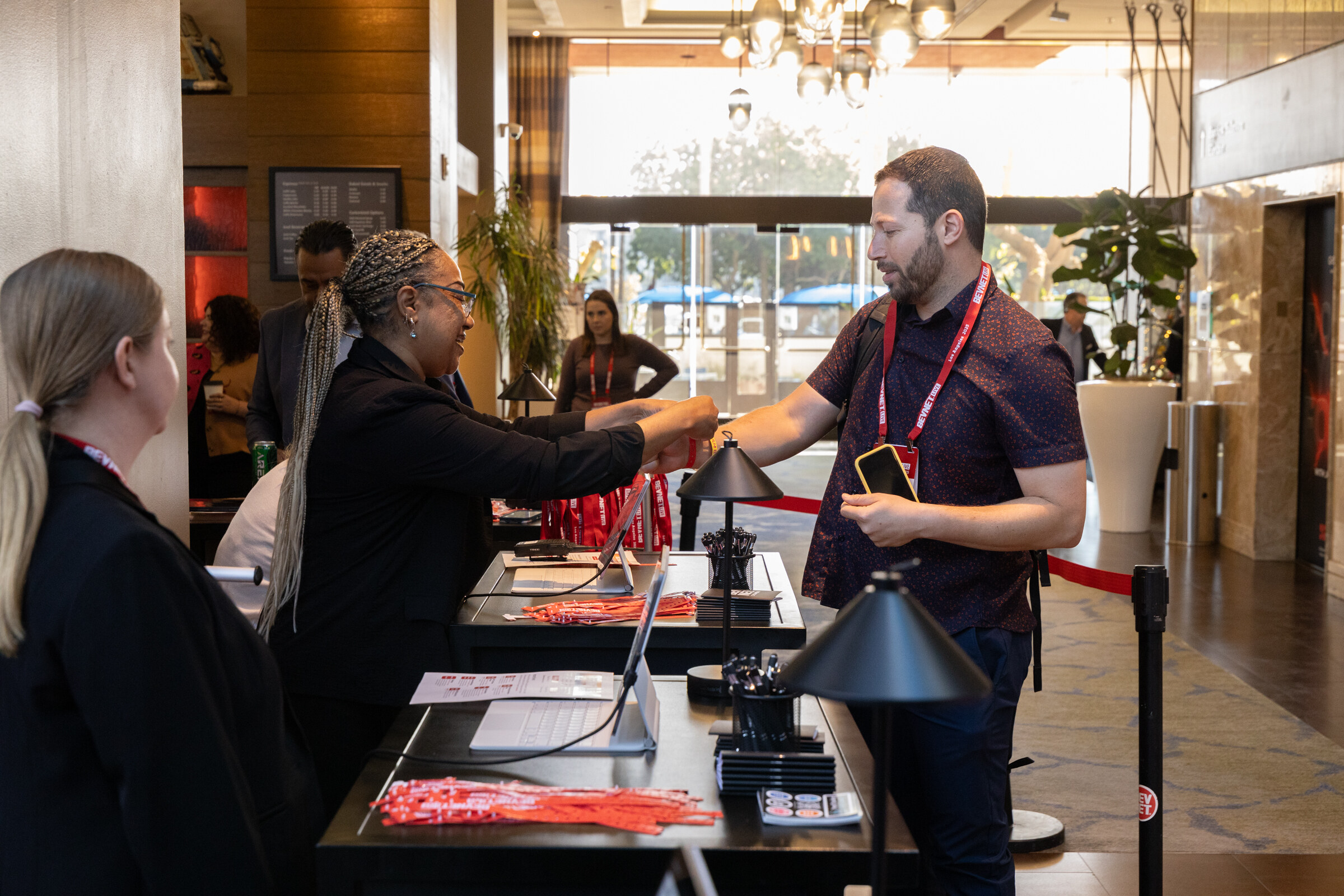 A man with a lanyard checks in at a registration desk while staff hand over badges.