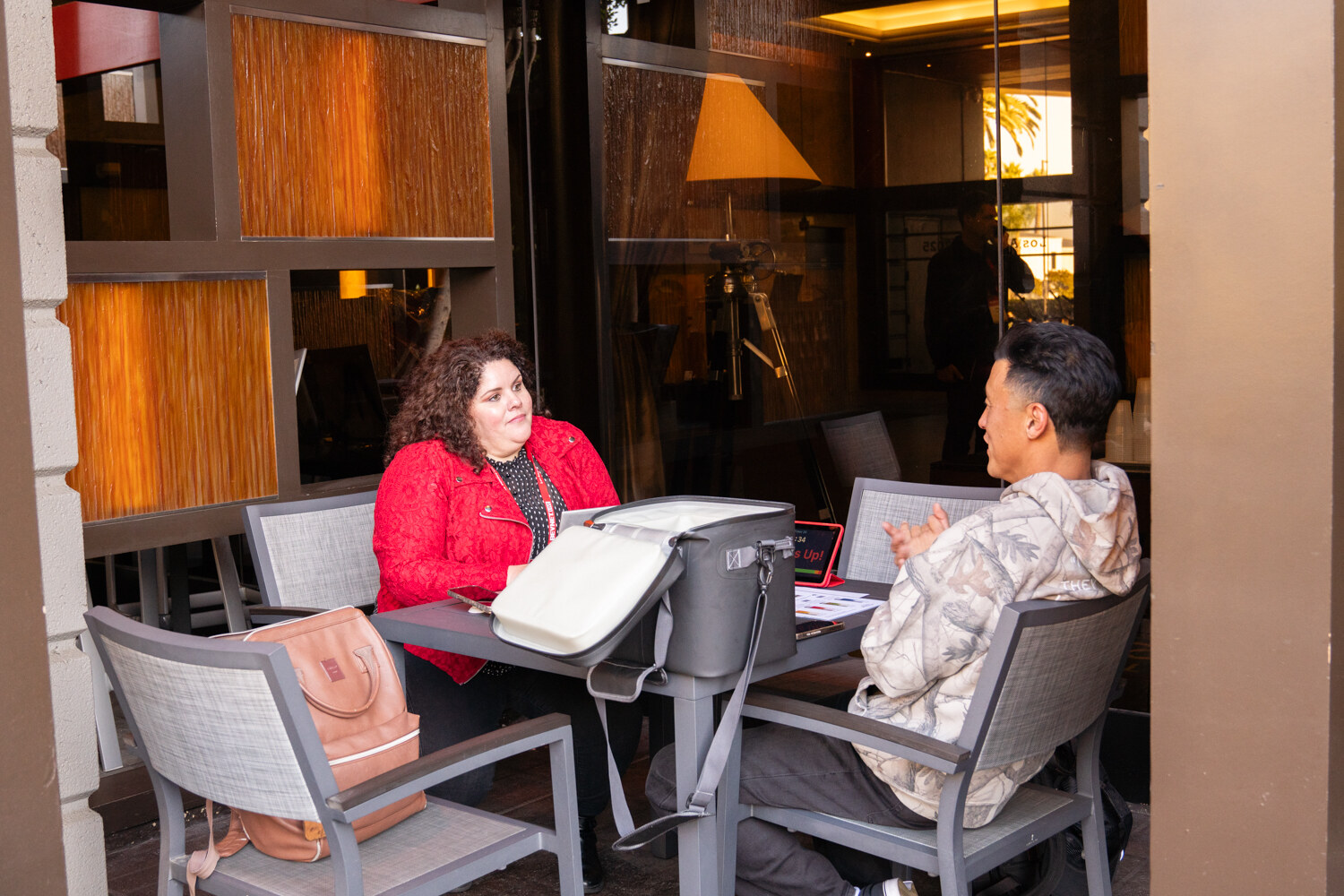 A woman in a red jacket and a man in a patterned jacket sit with a laptop.