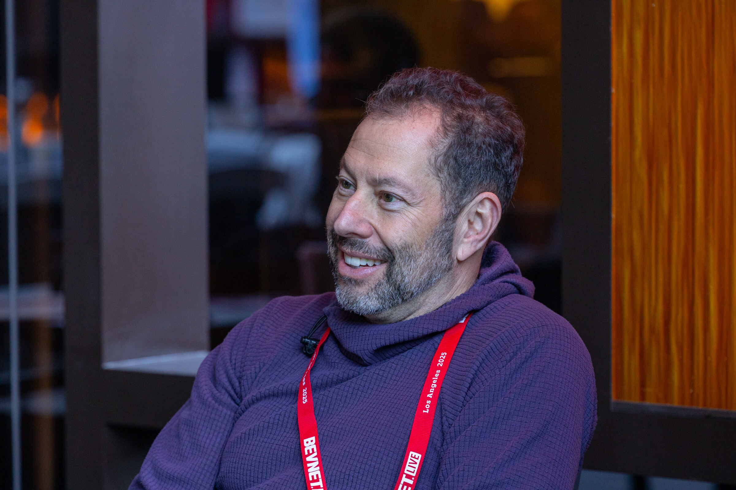 A bearded man in a purple hoodie smiles at a table.