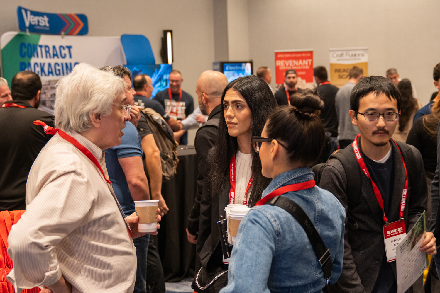 Attendees with coffee talk in front of exhibitor tables.