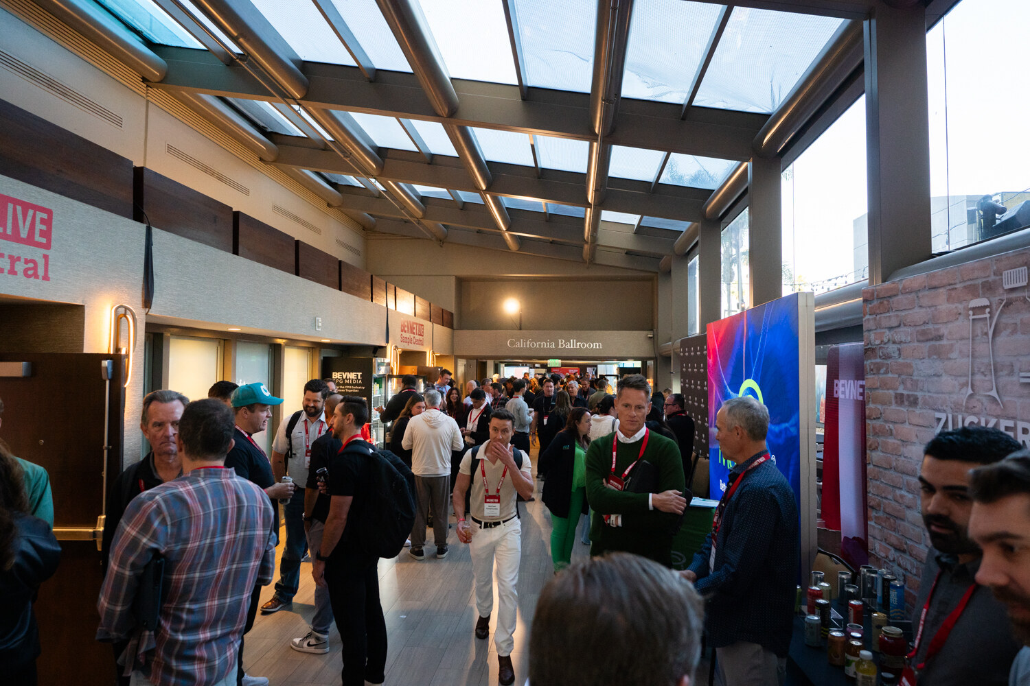Attendees fill a skylit promenade past sponsor displays.
