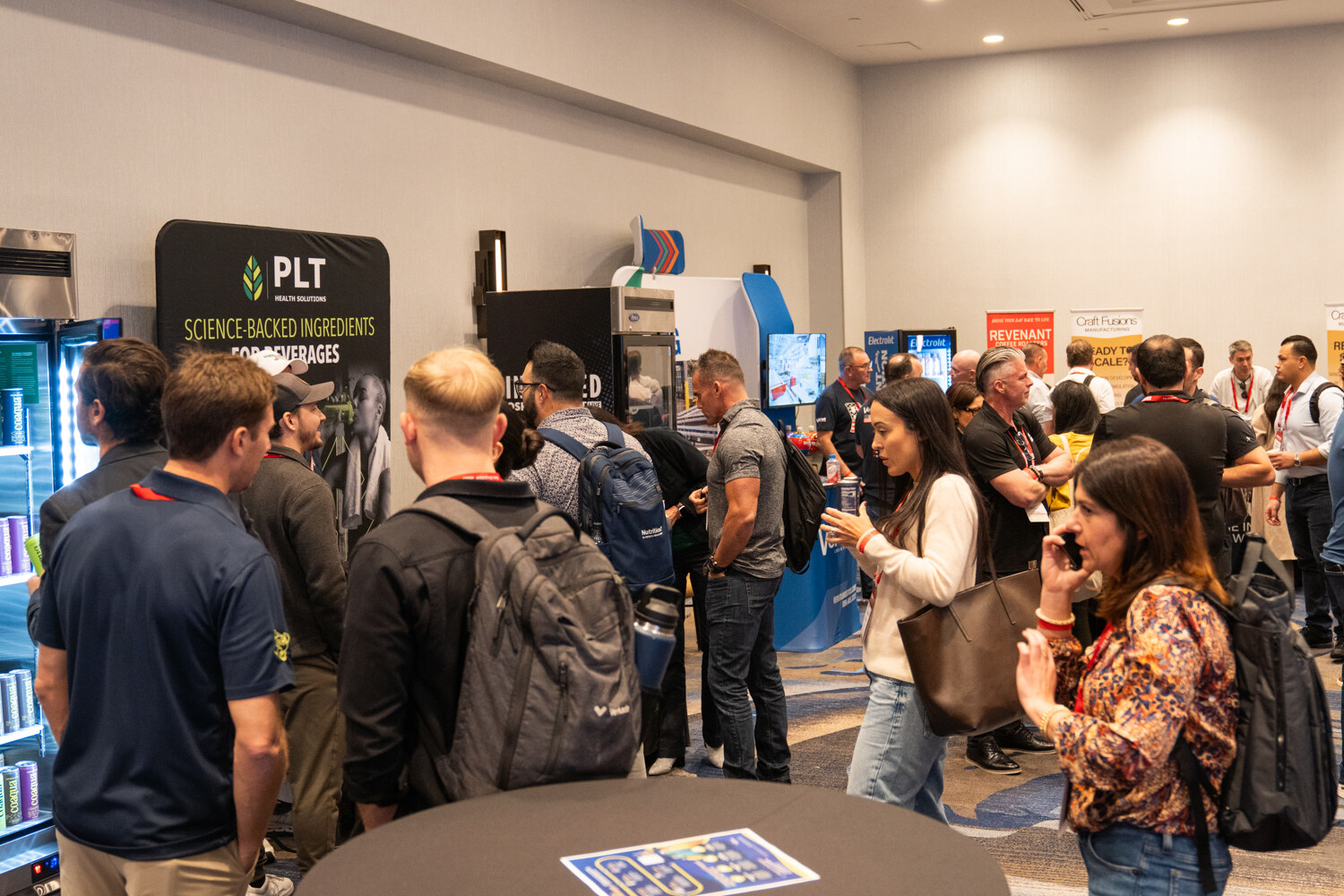 Attendees crowd around cocktail tables near a PLT banner.
