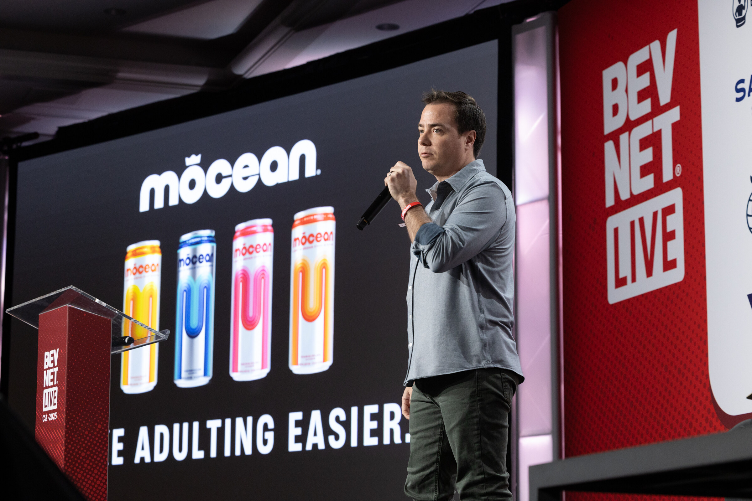 A man holding a microphone stands beside a Mocean slide reading Make Adulting Easier.