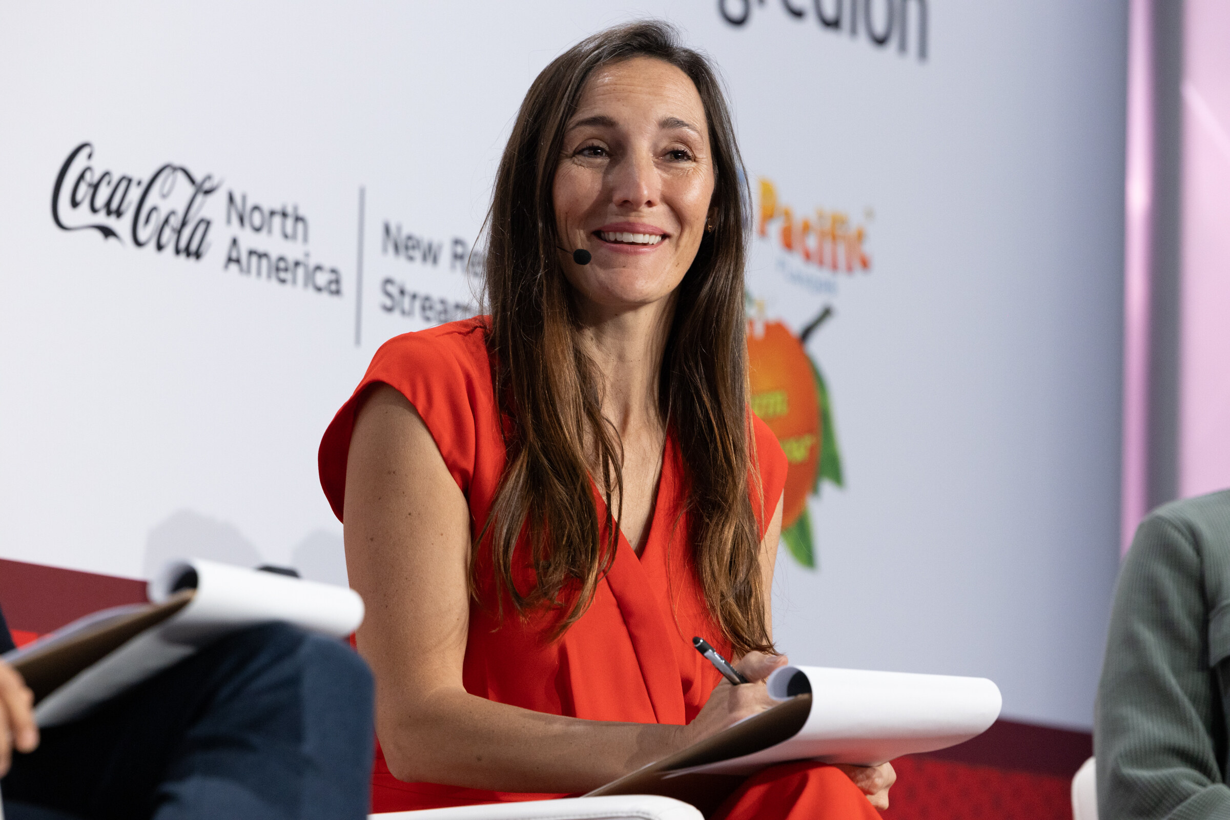A woman in a red dress smiles while taking notes on a pad.