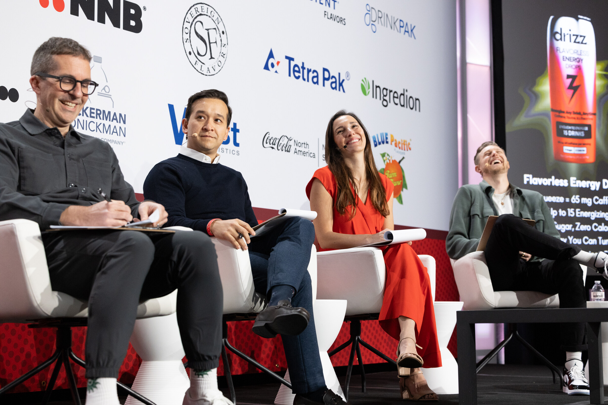 Four judges sit on stage, one laughing, as a presenter speaks.