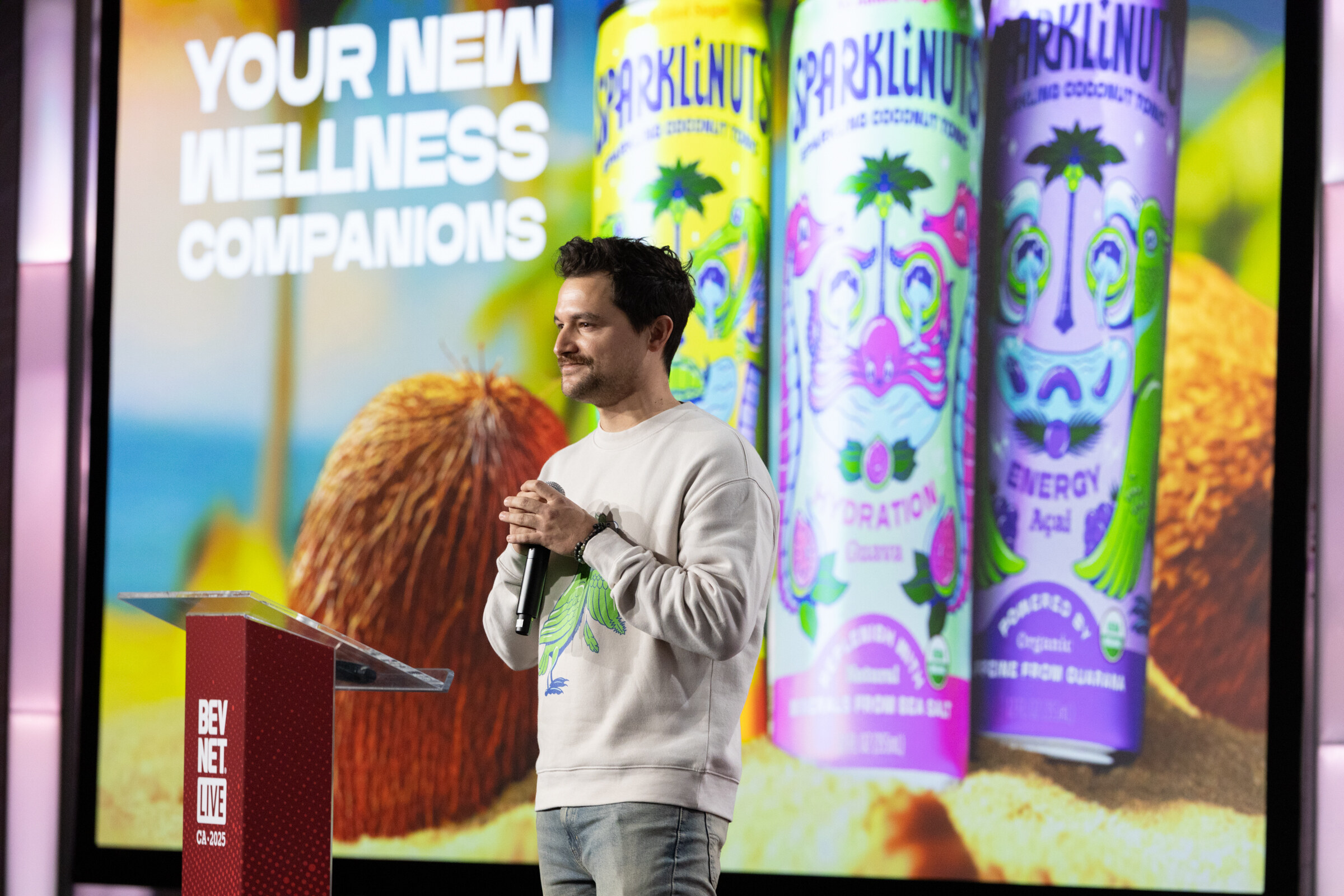 A man in a light sweater stands before a slide showing Sparklenut coconut drinks.