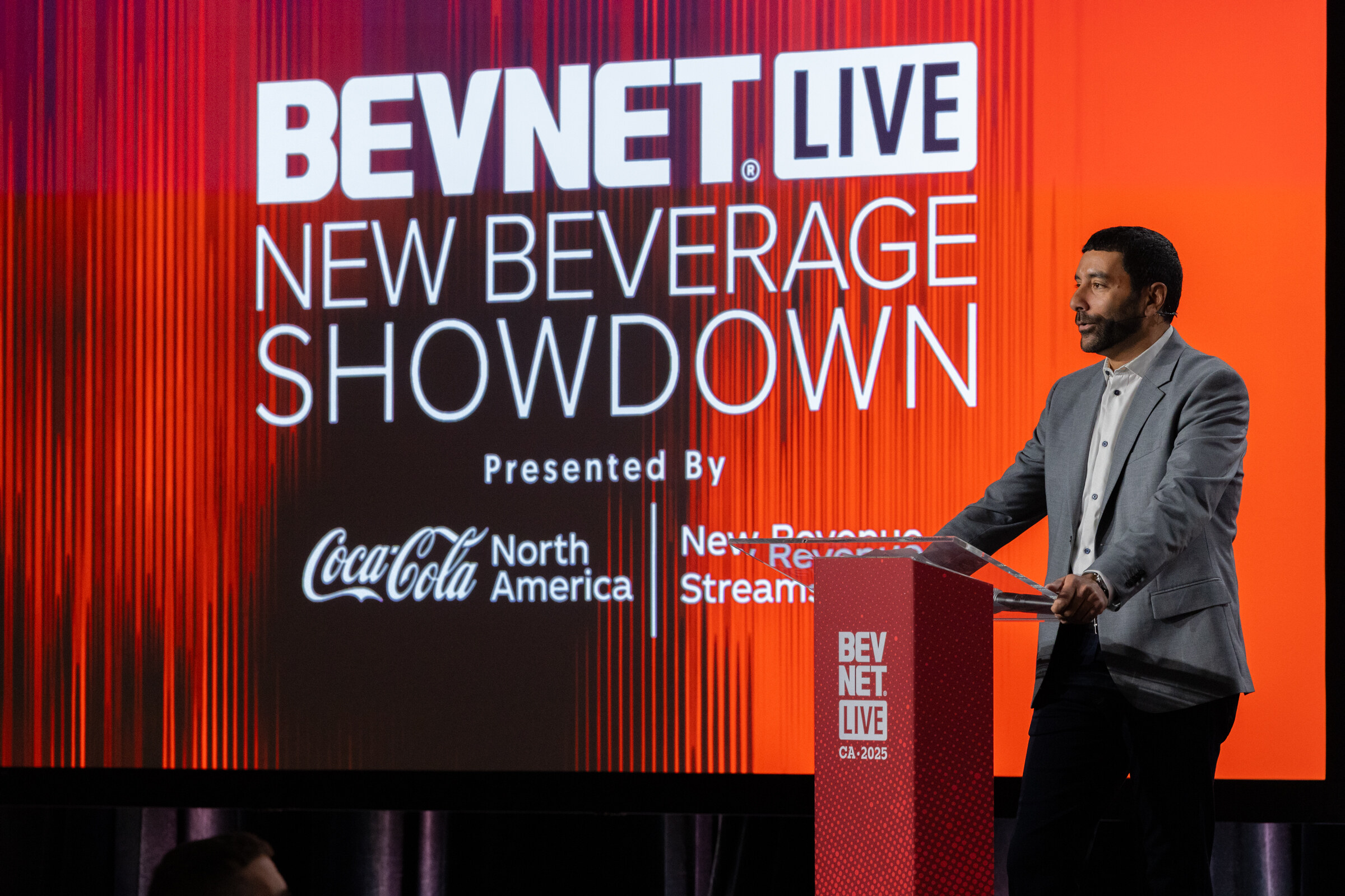 A man in a gray blazer stands at a podium in front of a New Beverage Showdown screen.